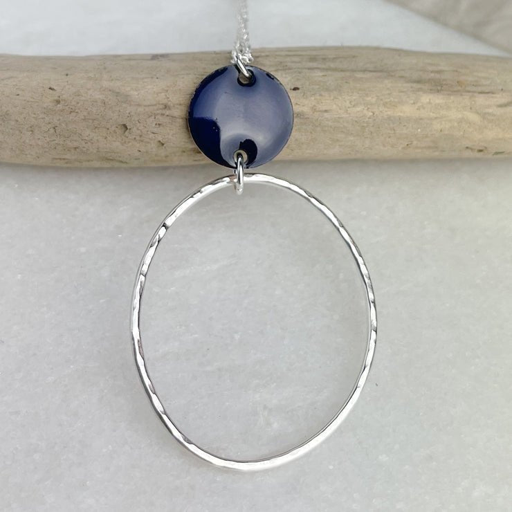 Navy blue ceramic disc pendant on silver chain above textured silver hoop of Mediterranean Blue Beaten Oval Hoop Necklace