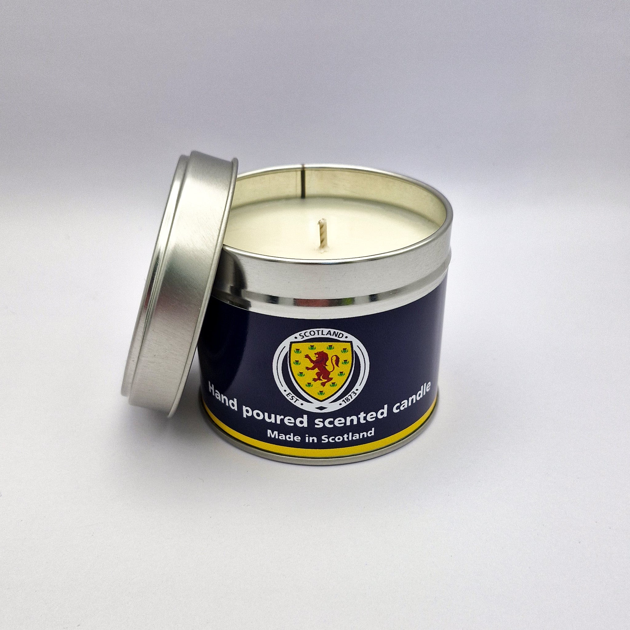 A navy blue and yellow scottish-themed hand-poured scented candle in a metallic travel tin container with lid slightly open
