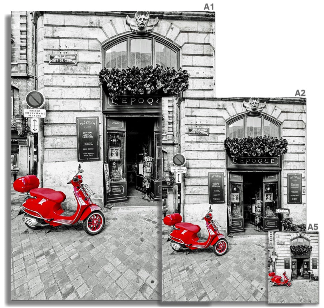 A vibrant red Bordeaux Vespa scooter with glossy finish and chrome accents parked outside a black-and-white storefront
