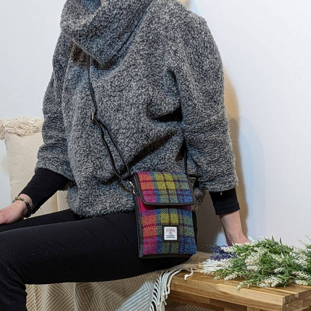 A colorful plaid harris tweed crossbody bag with black leather trim and a small white label.