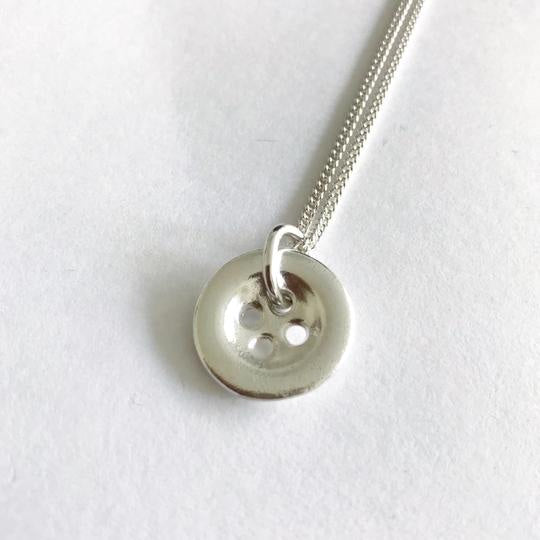 Silver button-shaped pendant necklace with polished finish and four holes