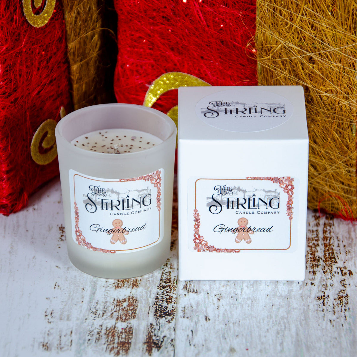 Frosted glass candle with a white box labeled "Gingerbread" beside it, set against a festive red background.