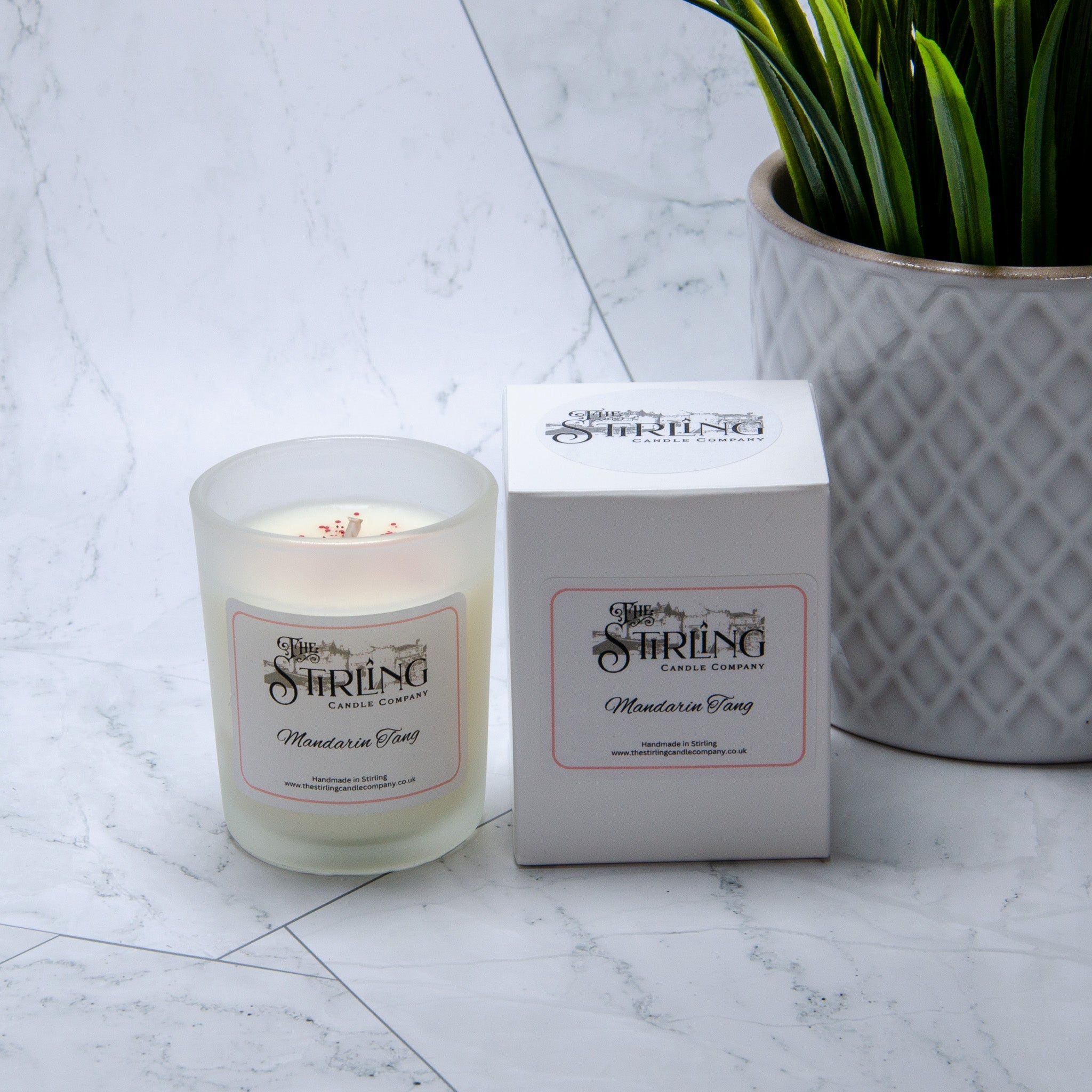 A frosted glass mandarin tang small candle with white wax and red flakes by Stirling Candle Company
