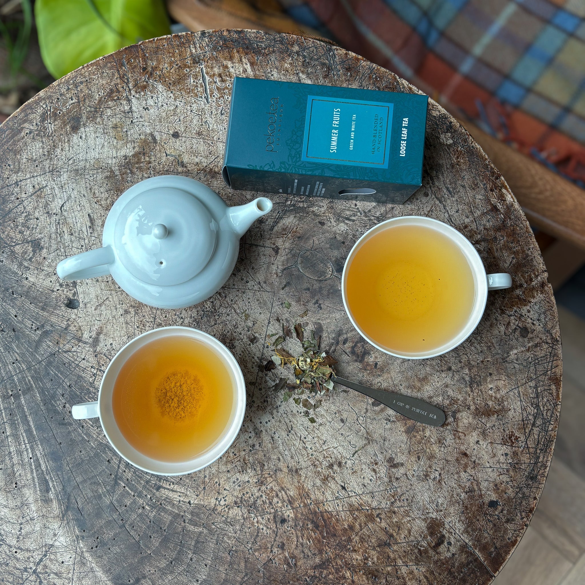 Light blue ceramic teapot with rounded lid and spout on rustic wooden table beside two white tea cups summer fruits