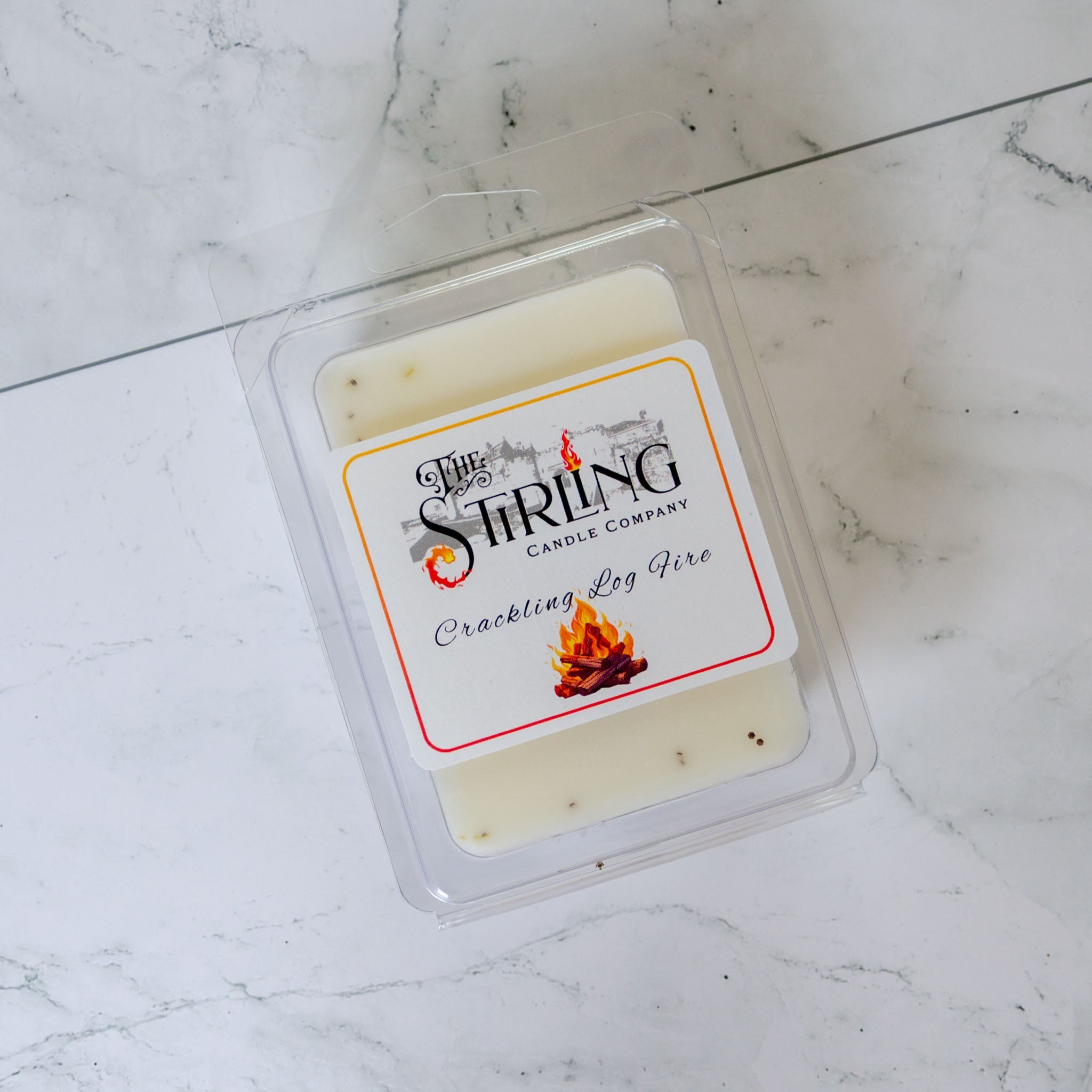 A creamy white crackling log fire wax melt clamshell in a clear plastic container from Stirling Candle Company