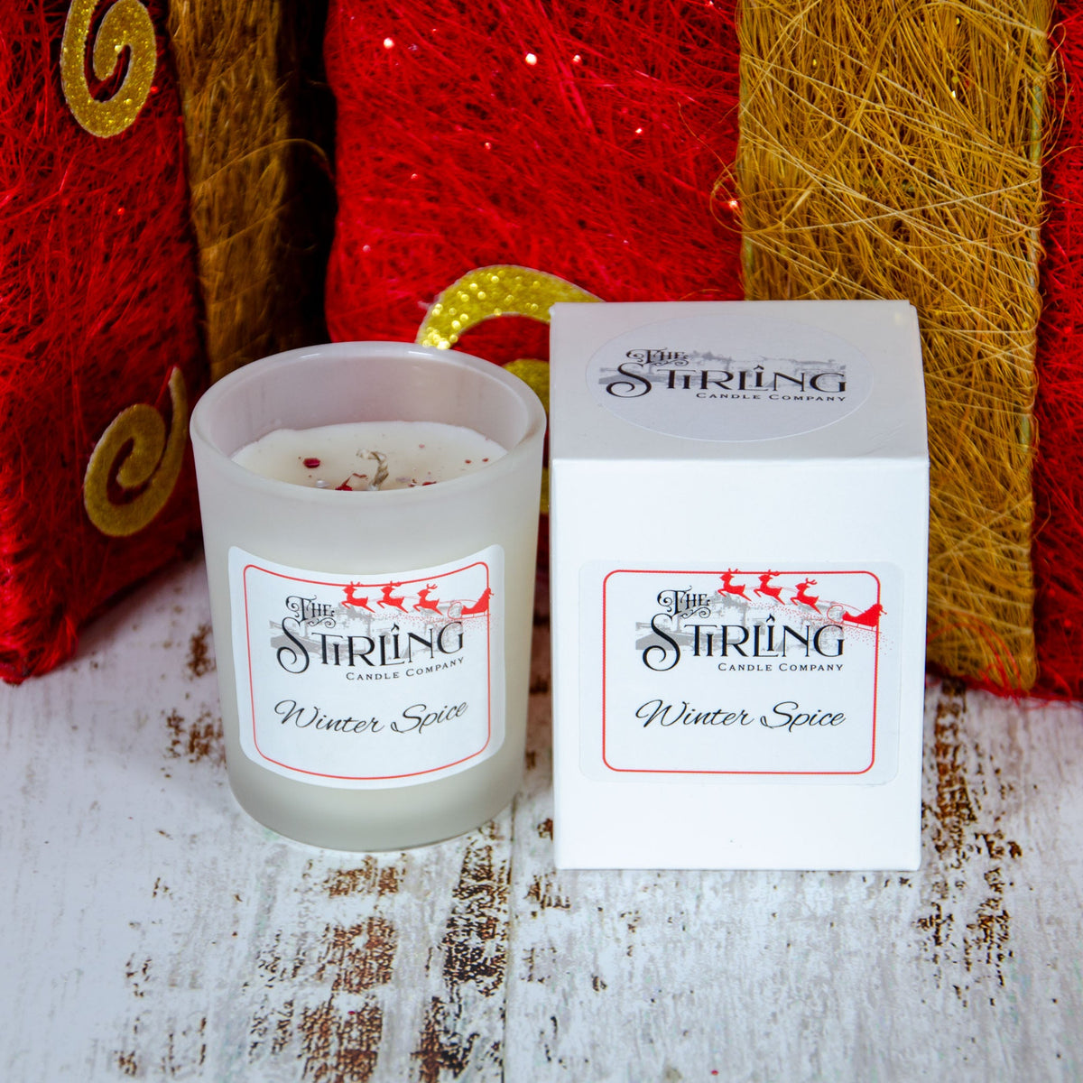 Frosted glass candle with a white label, beside a white box, set against a festive red background.