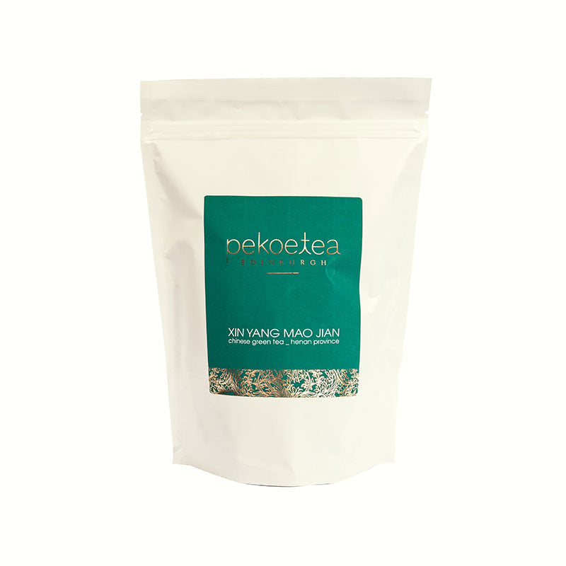 A white resealable pouch of Xin Yang Mao Jian Chinese green tea from Henan with a teal label and gold lettering