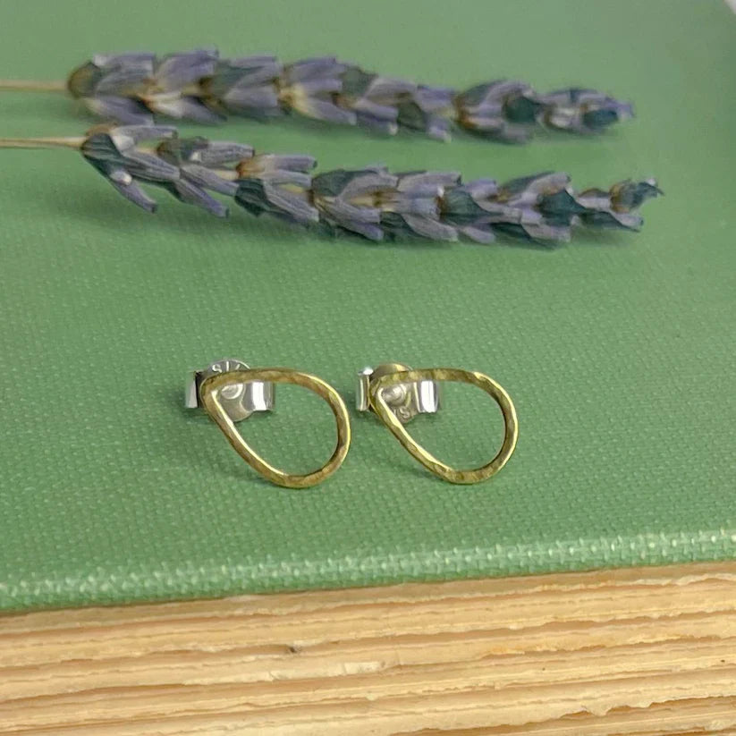 A pair of gold-toned brass teardrop stud earrings with hand-forged textured surface and silver-colored backings