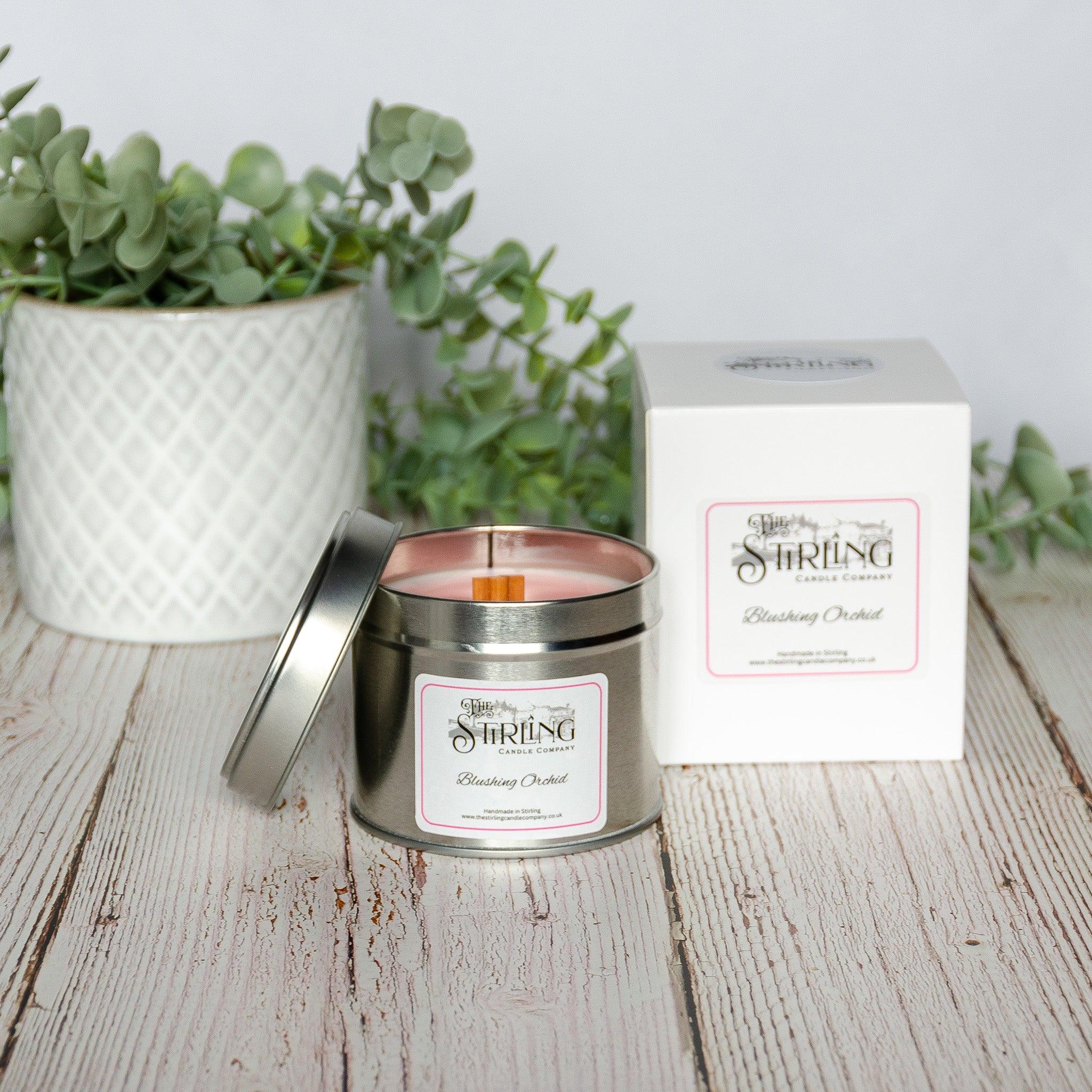 A sleek silver tin travel candle with pink wax and wooden wick labeled blushing orchid by the Stirling Candle Company