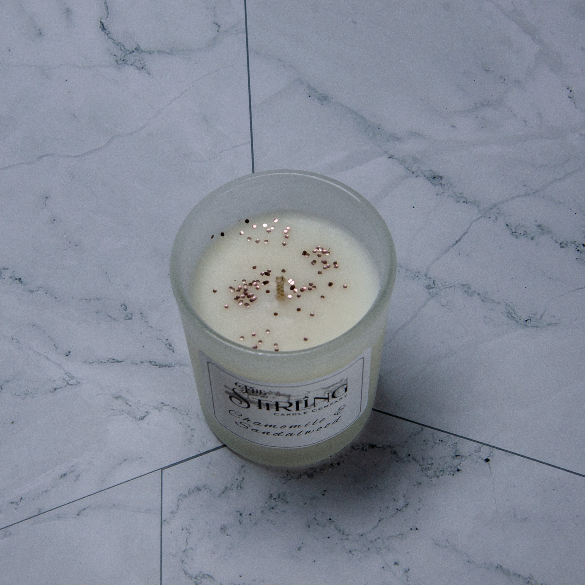 Small chamomile and sandalwood scented candle in frosted glass jar with rose gold and black glitter top