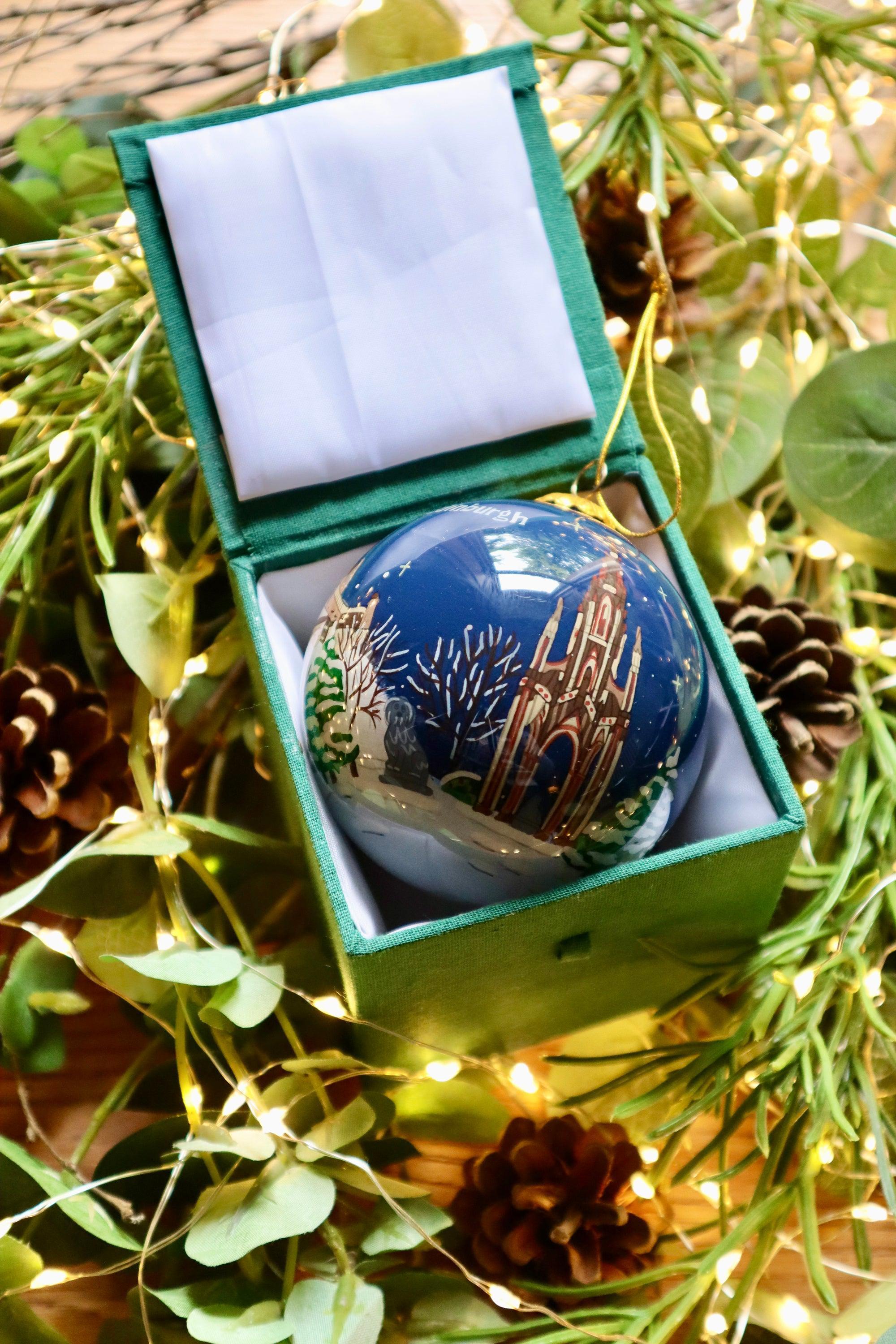 A glossy blue glass Christmas bauble with an illustrated cathedral in a green velvet-lined box for Edinburgh Christmas