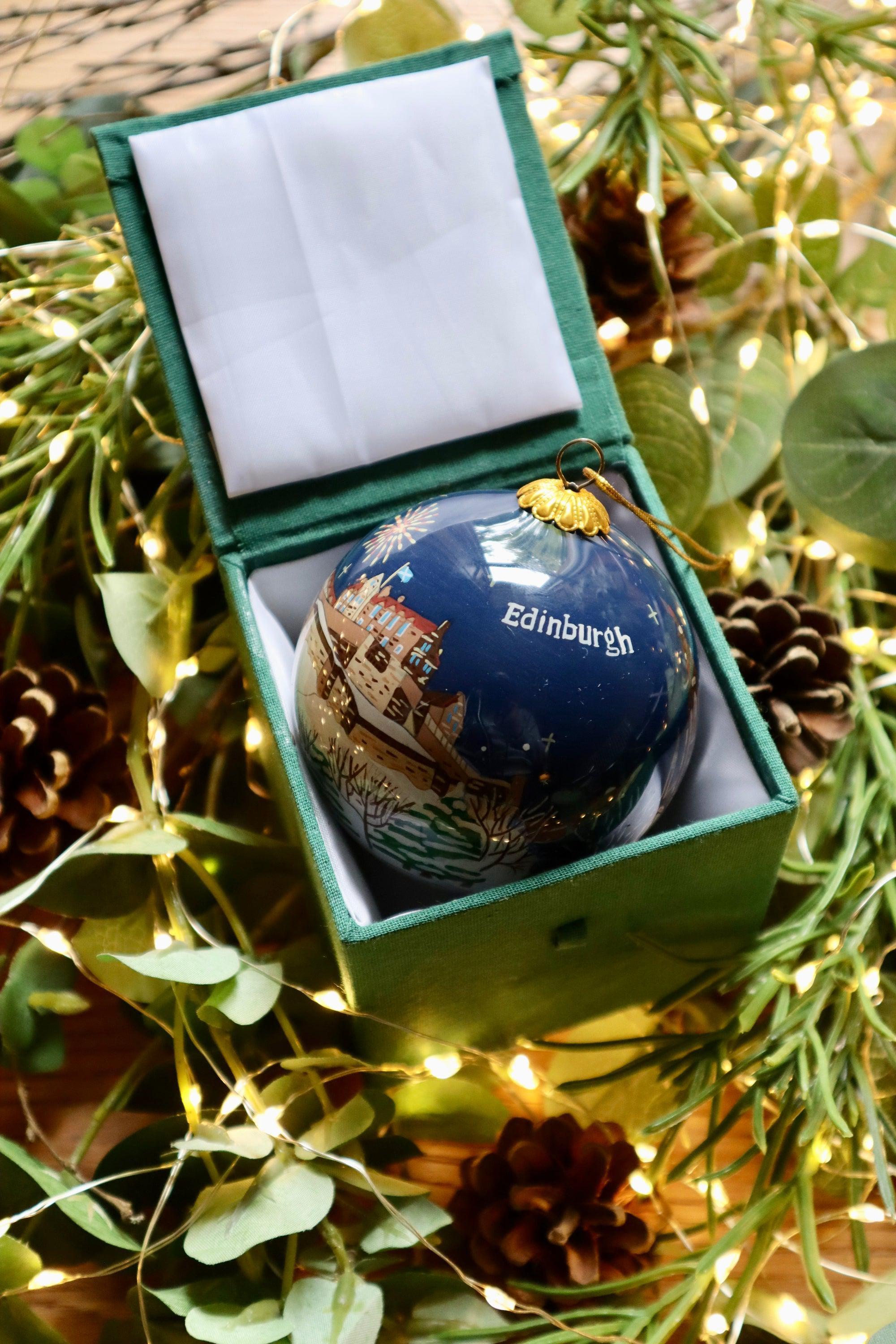 A navy blue glass edinburgh christmas decoration bauble with gold accents and white edinburgh text in a green box