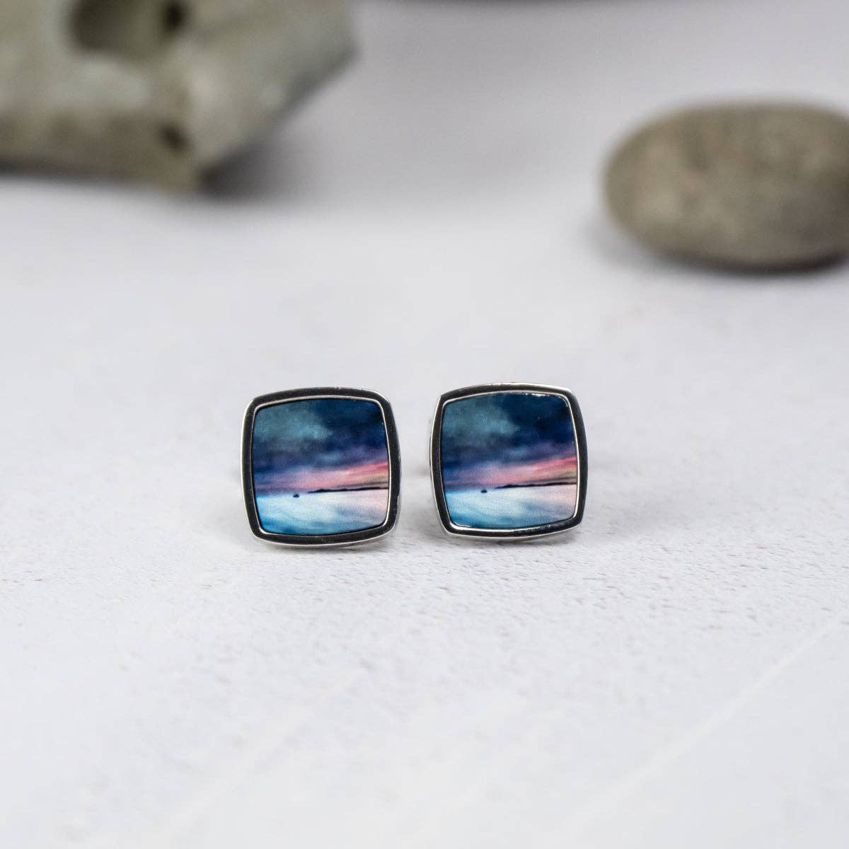 Square silver stud earrings with miniature painted sunset over water in deep blues, purples, pinks