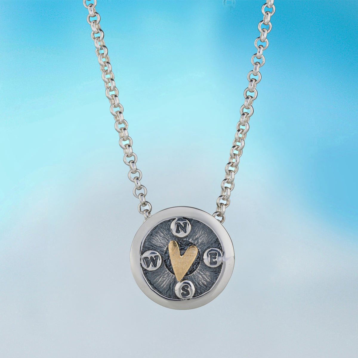 Silver and gold compass pendant necklace with textured face engraved with cardinal directions and central heart motif