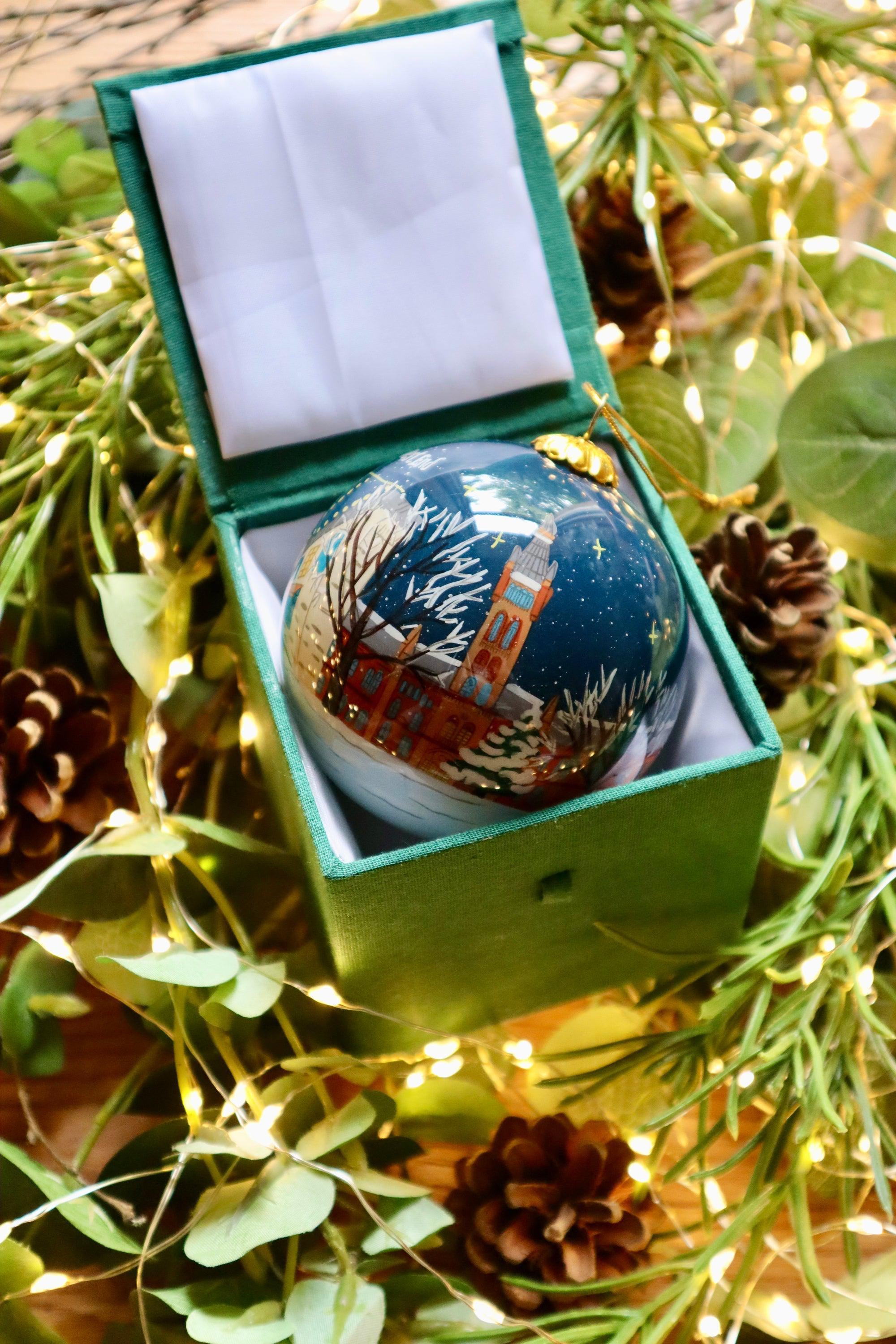 A glossy blue glass bauble with a detailed winter scene in an elegant green velvet-lined box for Scottish Christmas
