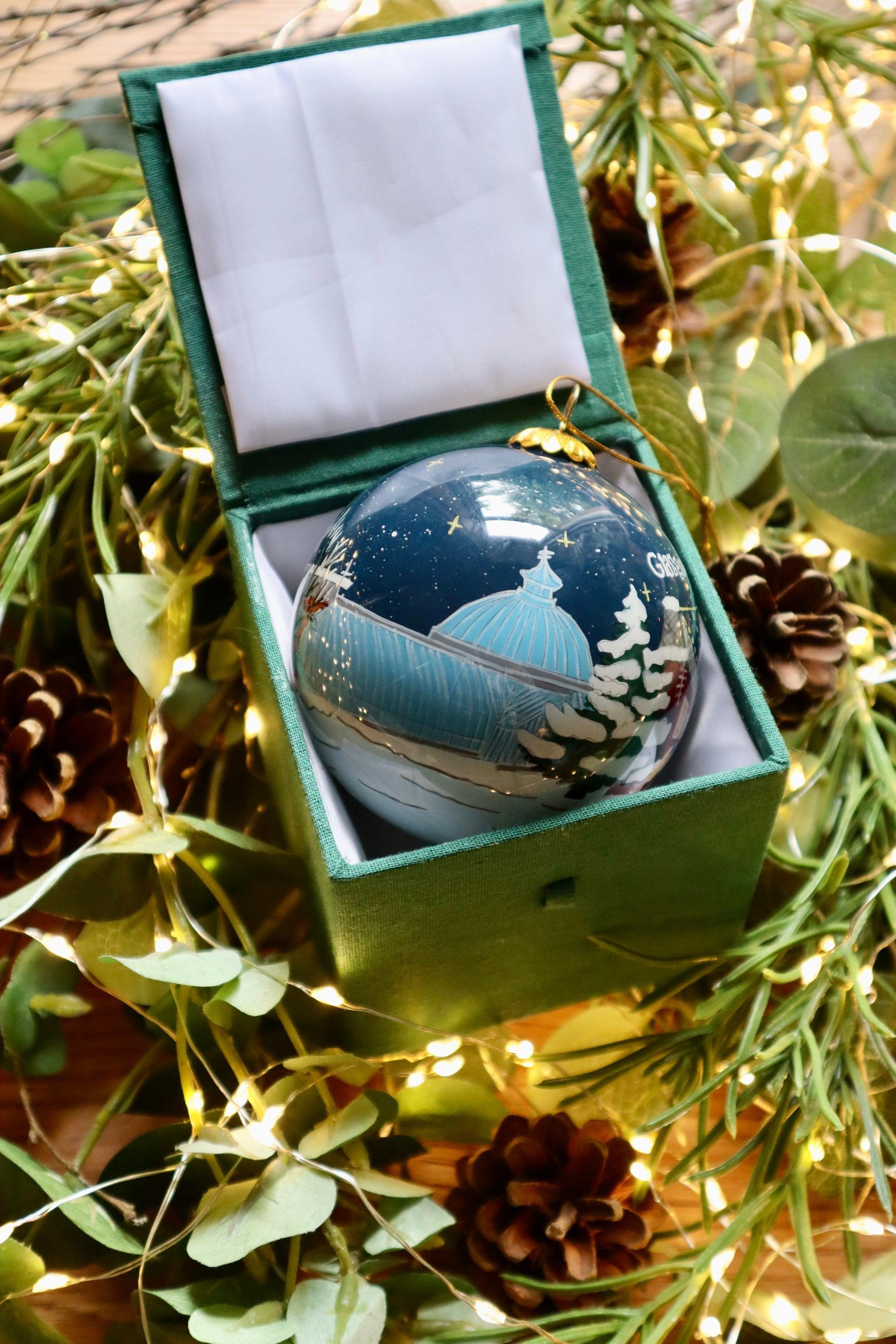 A clear glass Glasgow’s West End Christmas bauble with a painted blue-domed building in a green velvet box