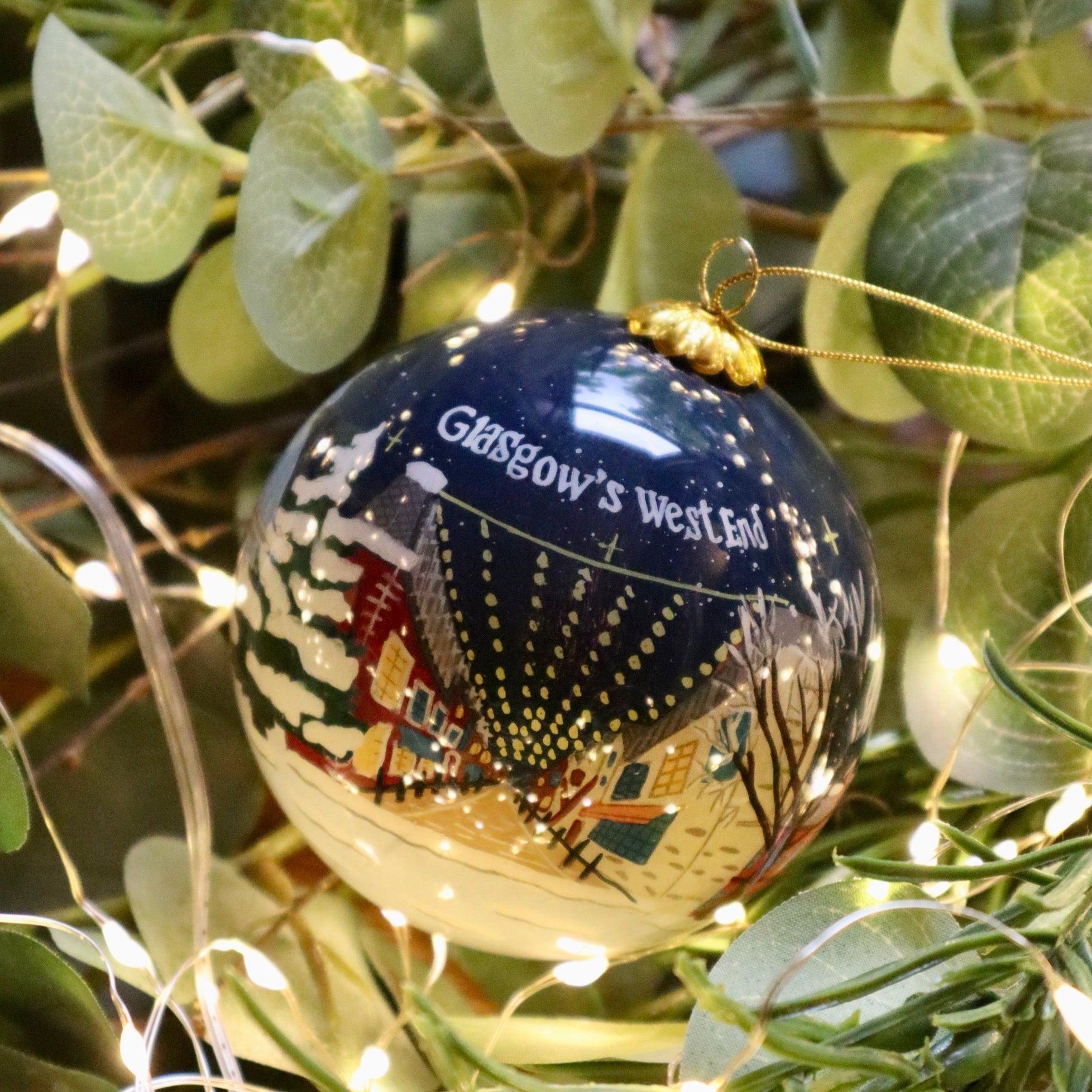 A glossy navy blue Christmas bauble with a painted snowy Glasgow West End scene and a gold hanging loop