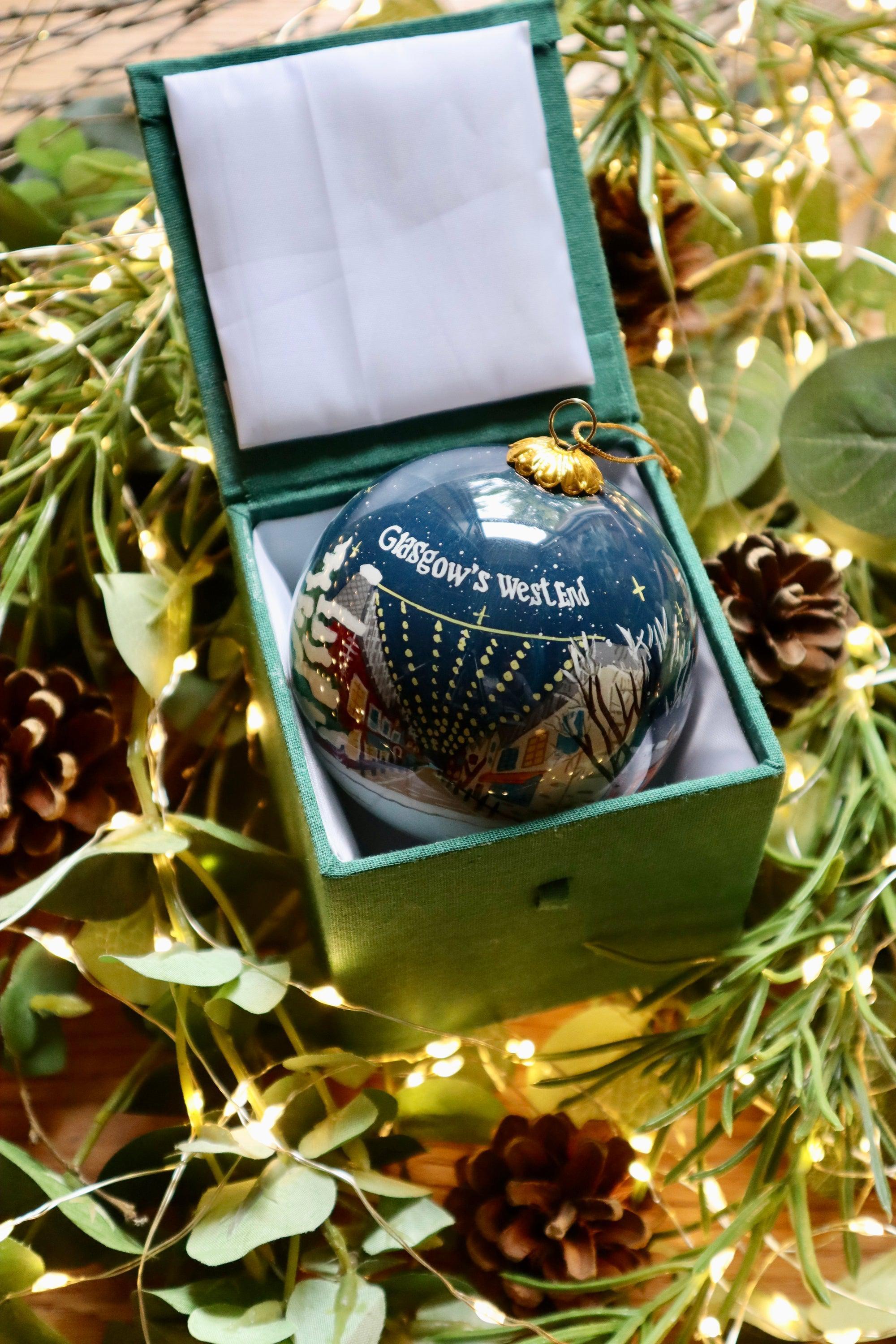 A glossy dark blue glass Christmas bauble with a gold cap featuring an illustrated scene of Glasgow’s West End