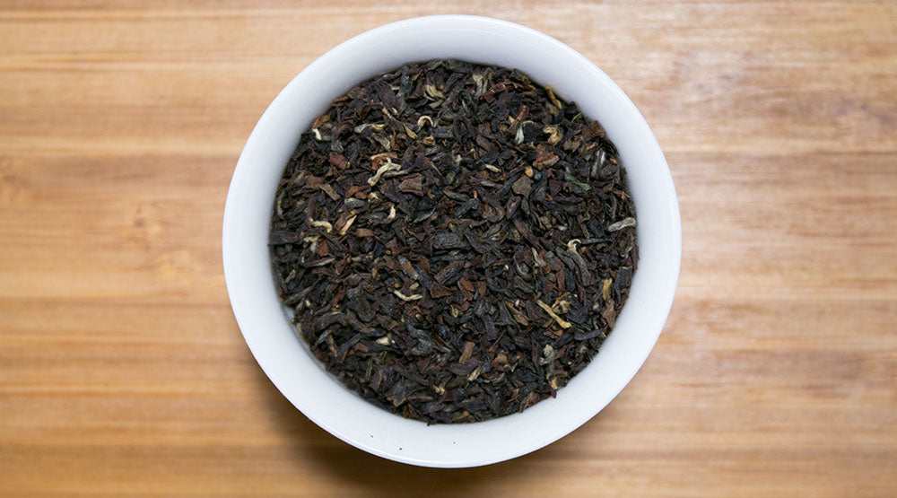 A white ceramic bowl filled with dark crumbled loose leaf gopaldhara tgbop second flush darjeeling tea leaves