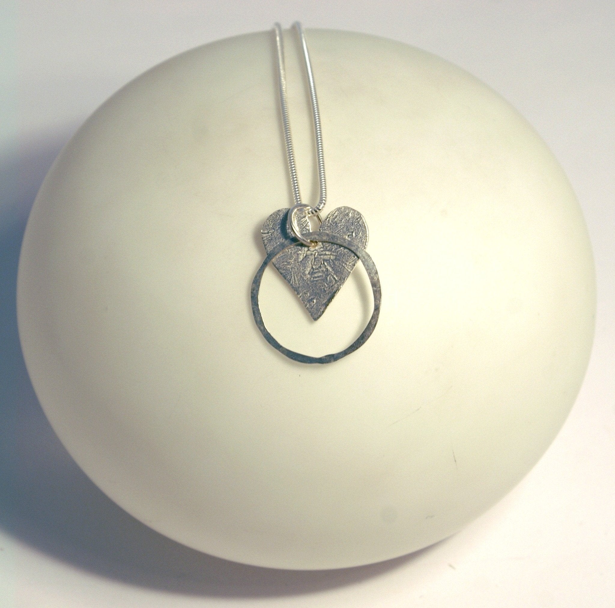 Silver heart pendant necklace with textured layered design and circular ring element for stylish wear