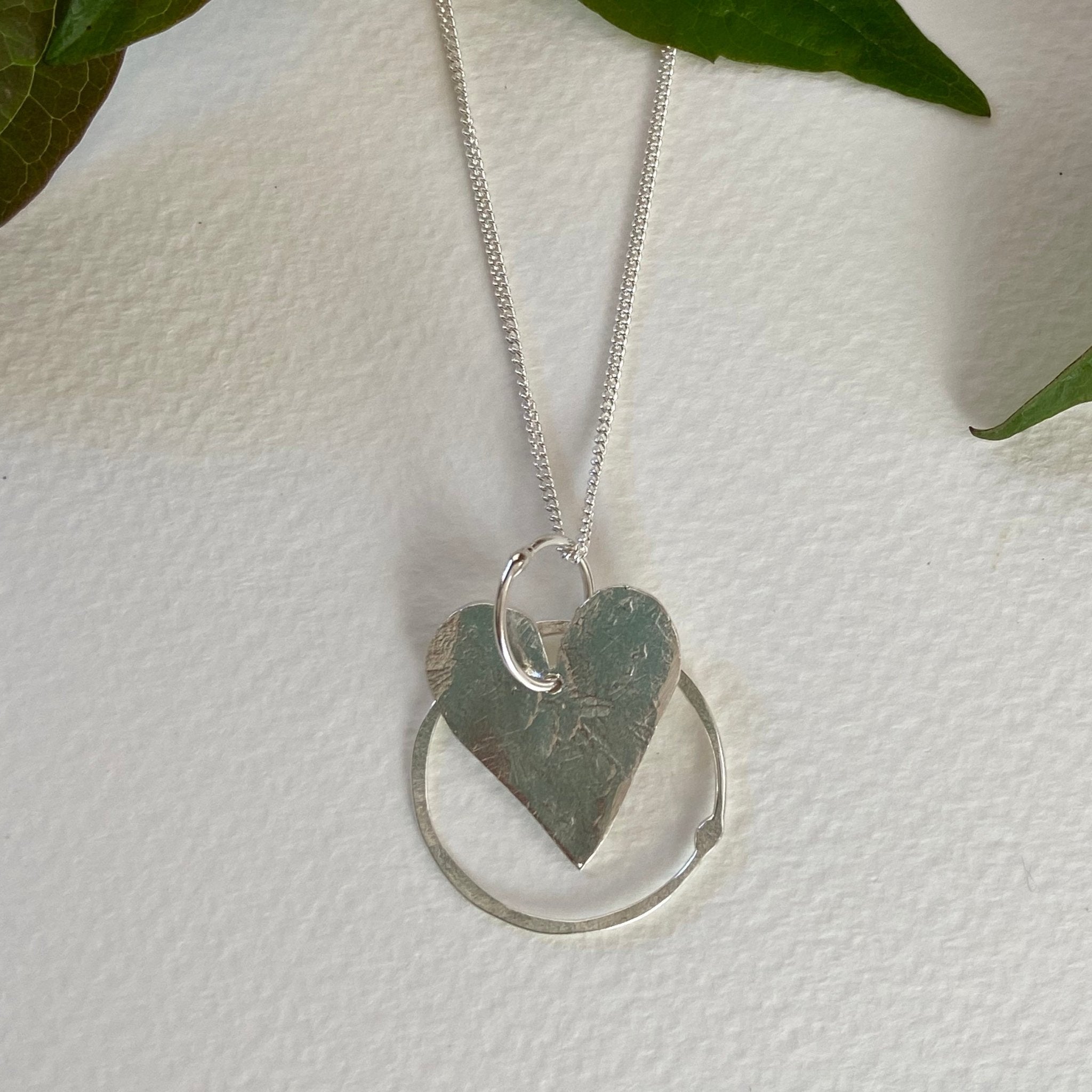 Silver heart hoop pendant with hammered texture suspended from delicate chain framed by open circular ring