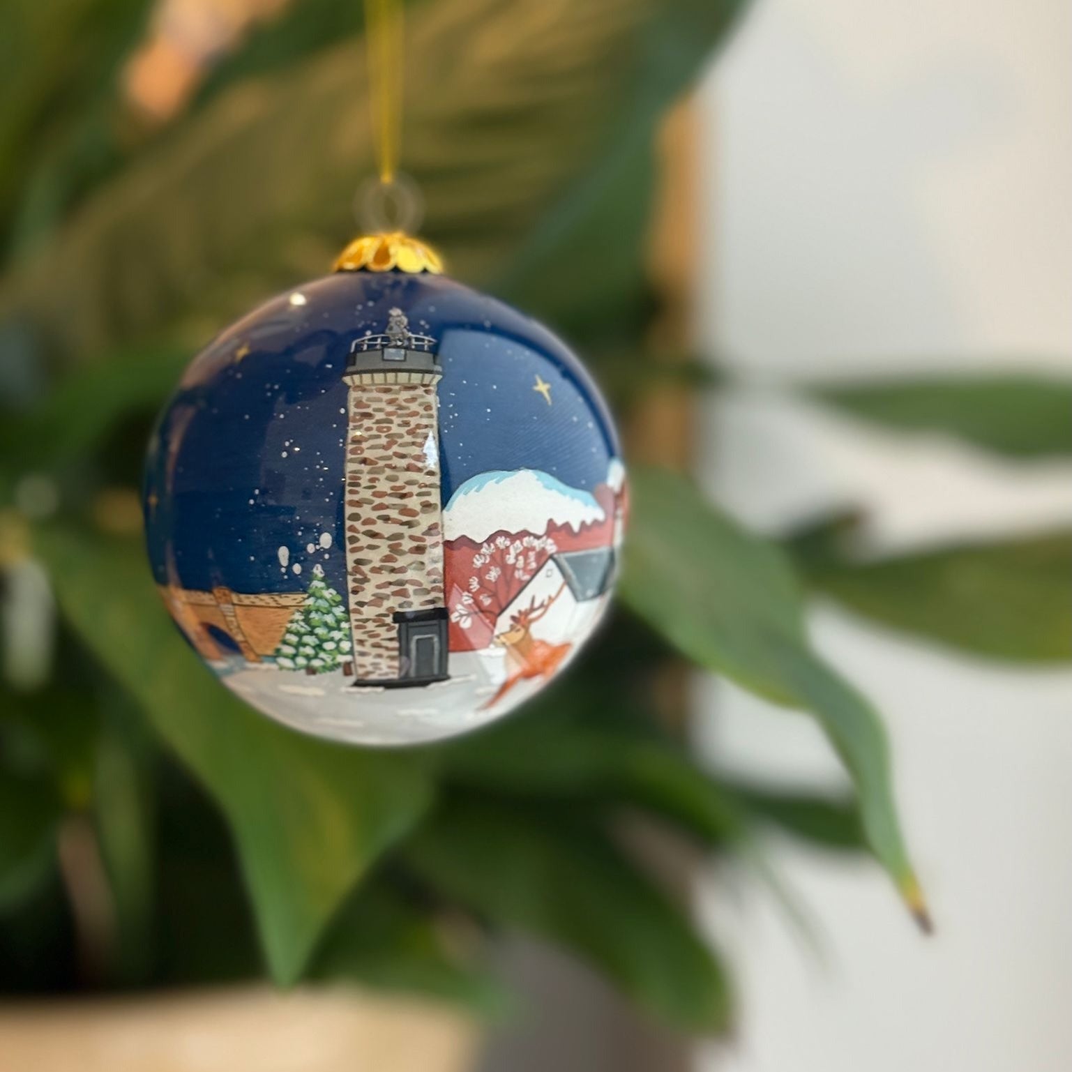 Blue glass christmas bauble featuring a painted stone lighthouse scene with snow trees and deer for scottish decor