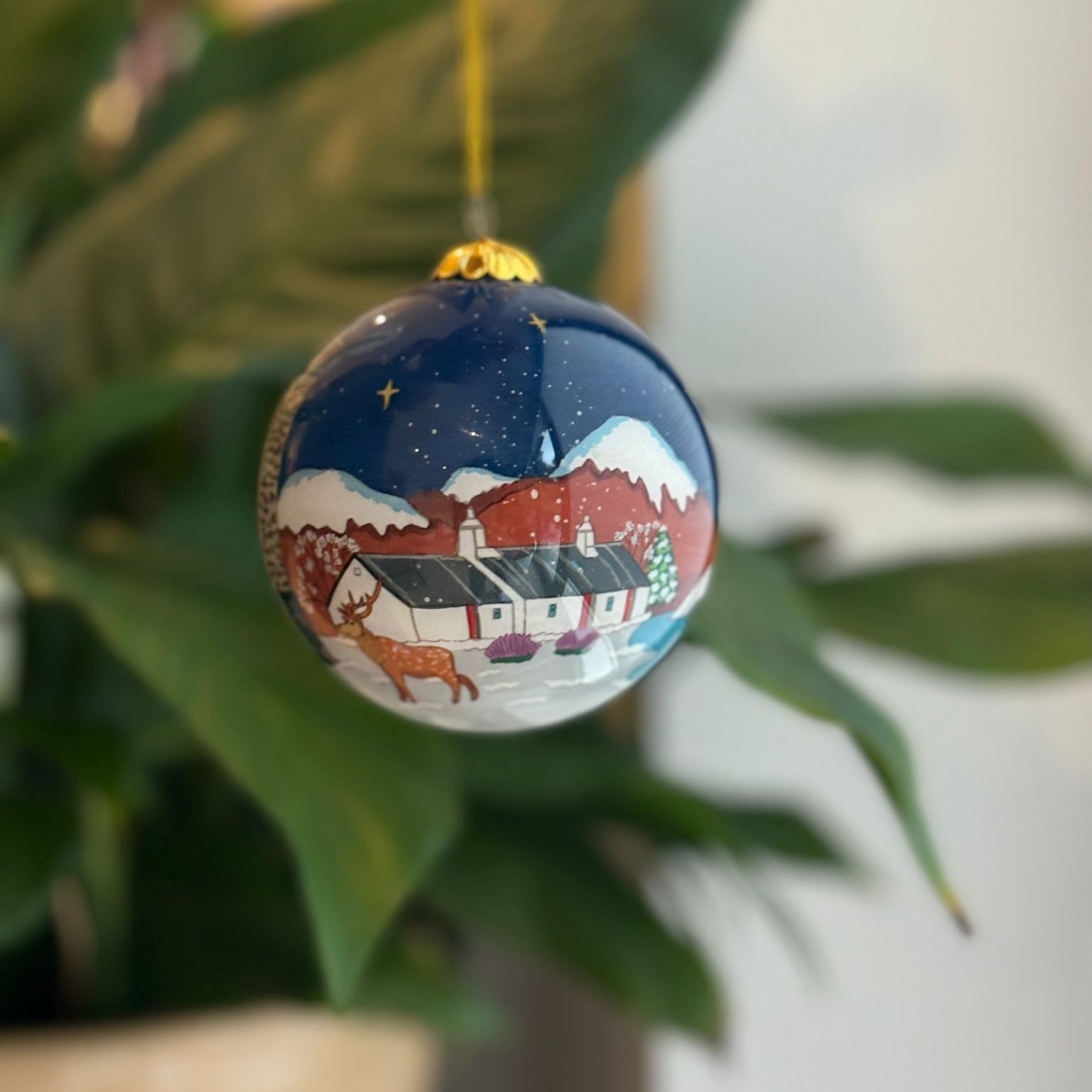 A hand-painted navy blue glass christmas bauble featuring a snowy village scene from the highlands collection