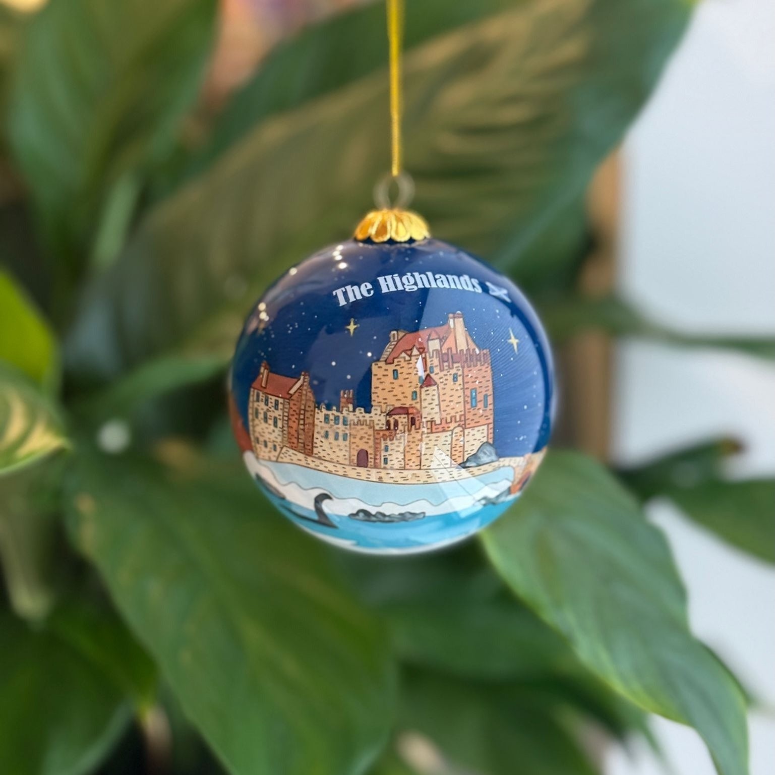 A glossy blue glass christmas bauble featuring a detailed castle illustration and the highlands text under a starry sky