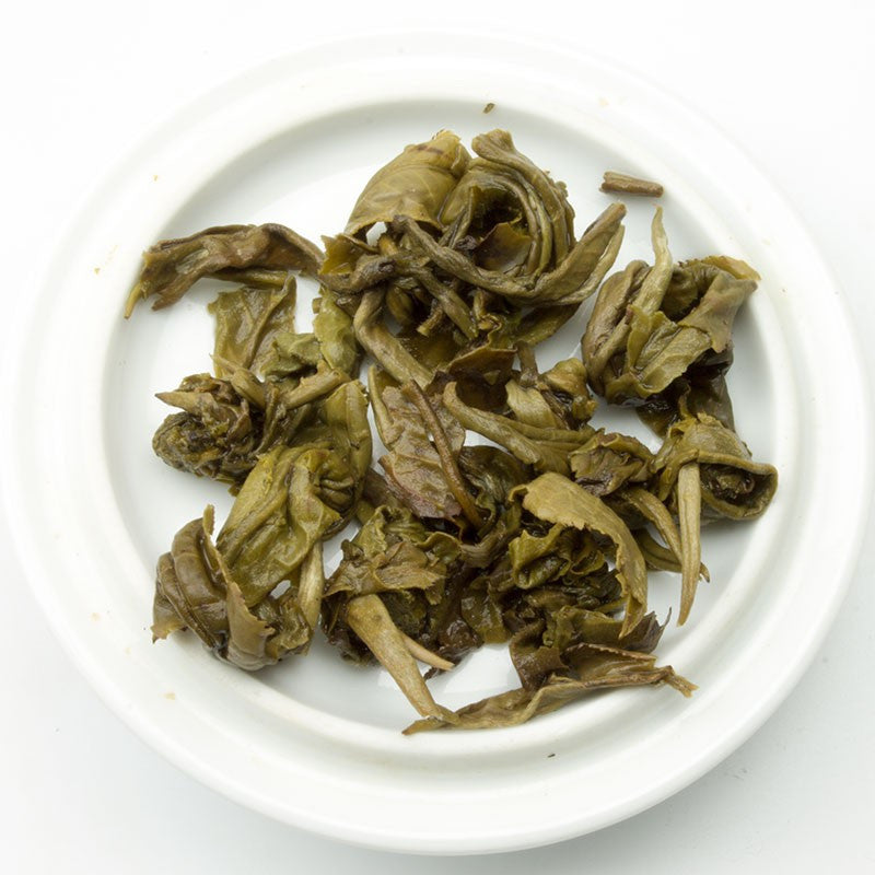 Dried twisted green jasmine dragon pearl tea leaves with brown edges in a white ceramic bowl for brewing