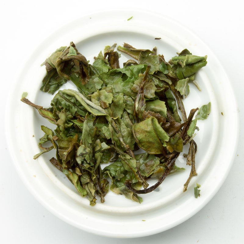 A pile of dried slightly curled green white tea leaves with hints of brown and white in pai mu dan white tea