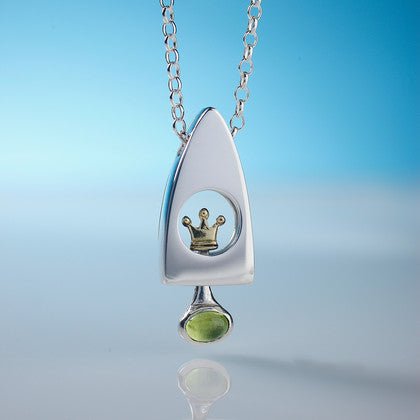 Silver princess and the pea pendant shaped like a rocket with a gold crown inset and green gemstone dangle