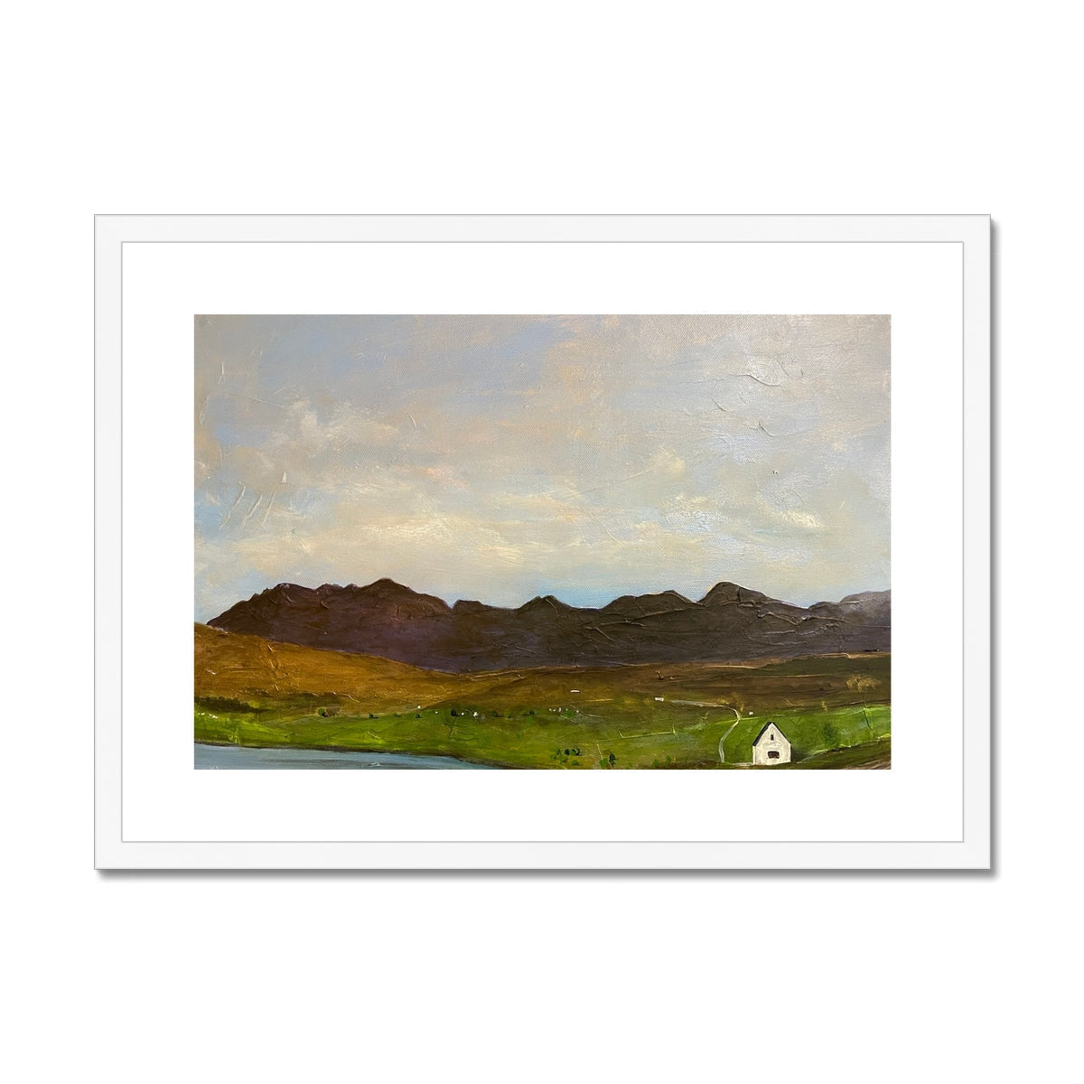White-framed art print of small white cottage in green fields before dark mountains