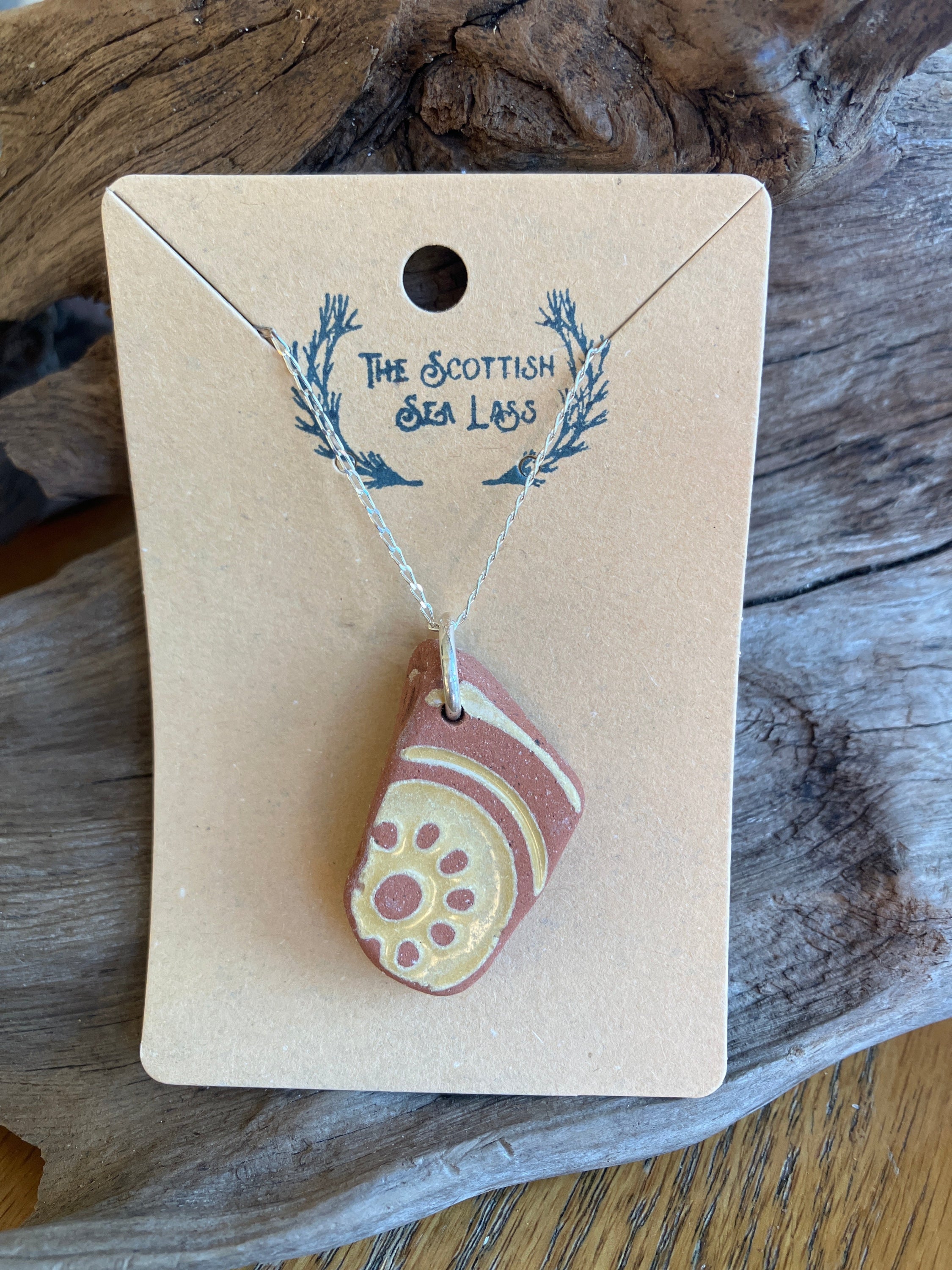 Reddish-brown ceramic shard pendant with cream designs on silver chain on light brown card