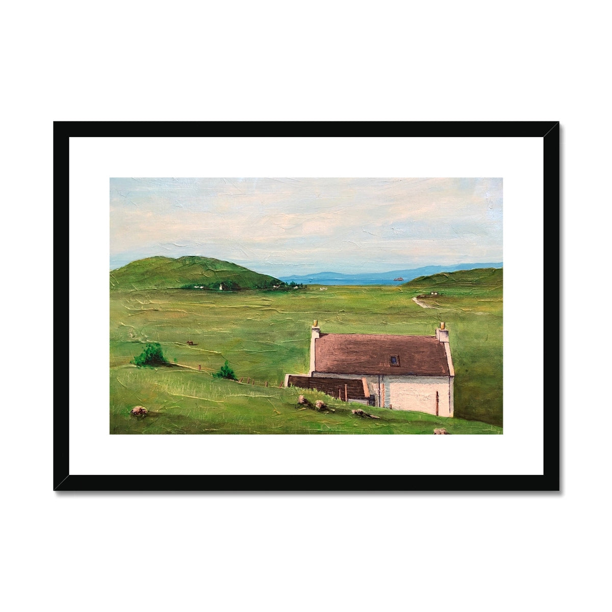 Framed landscape print of a white house with brown roof in green field with hills and water