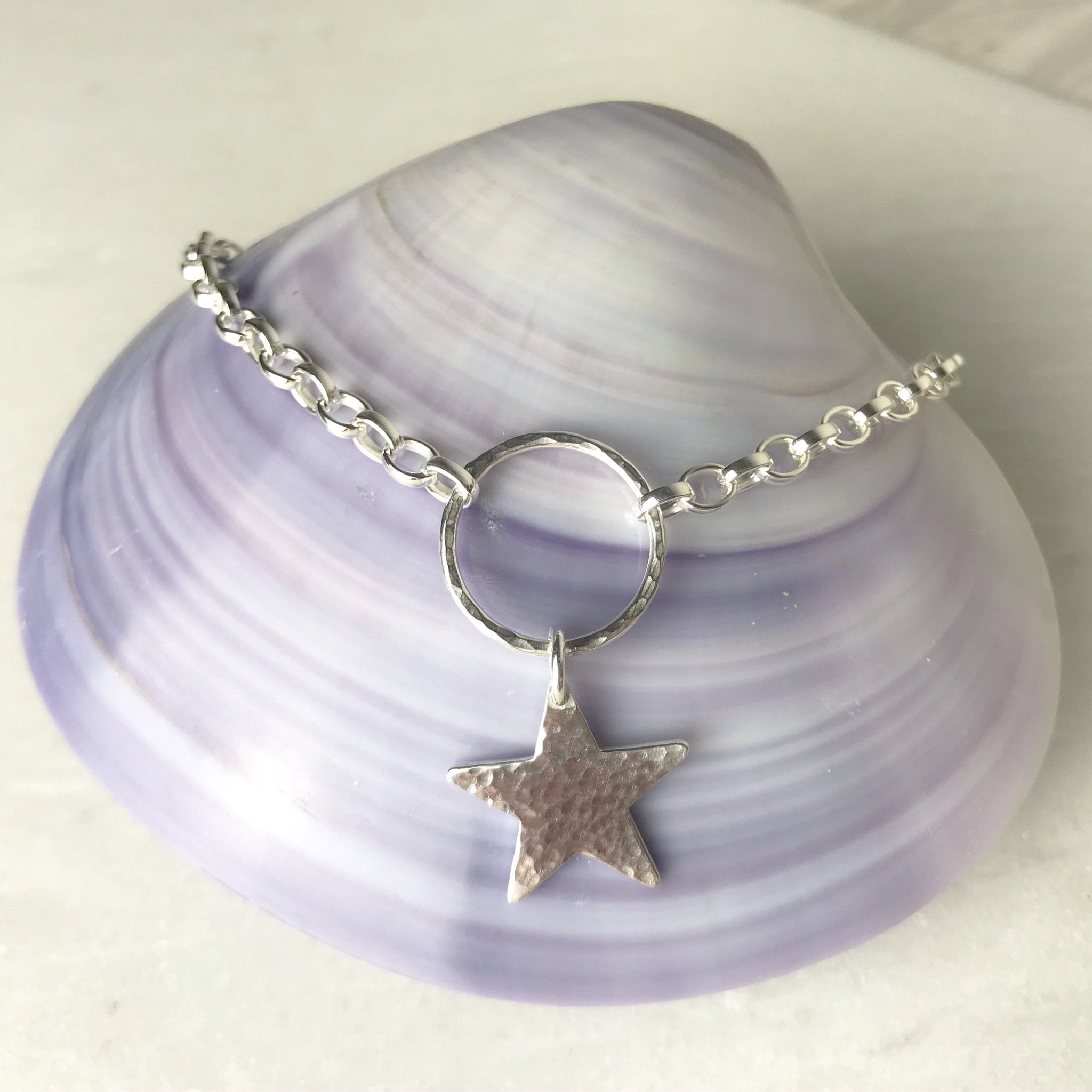Silver star charm bracelet with hammered texture on lavender seashell