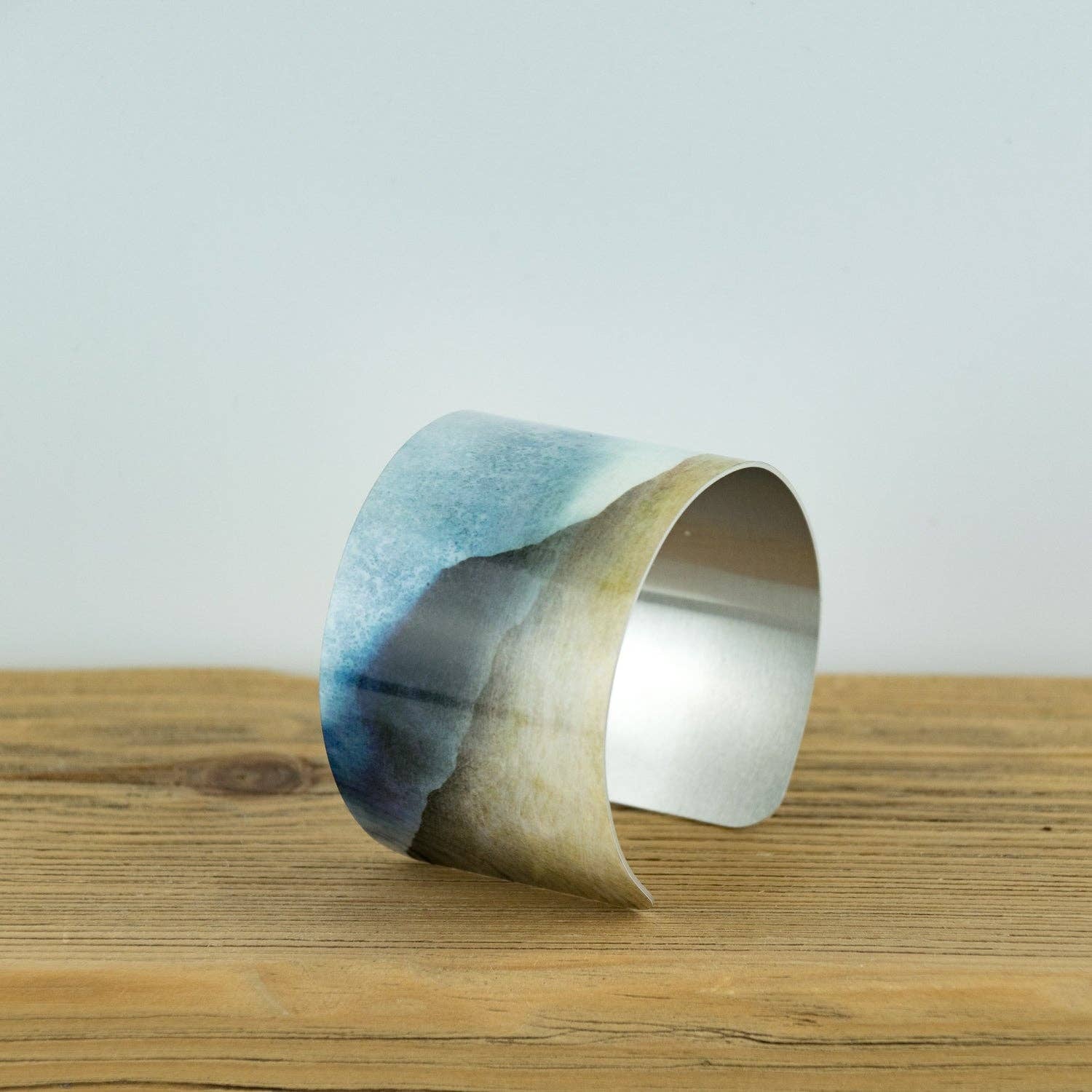 Sleek silver Glencoe aluminium bangle with blue-beige watercolor landscape design by Cath Waters