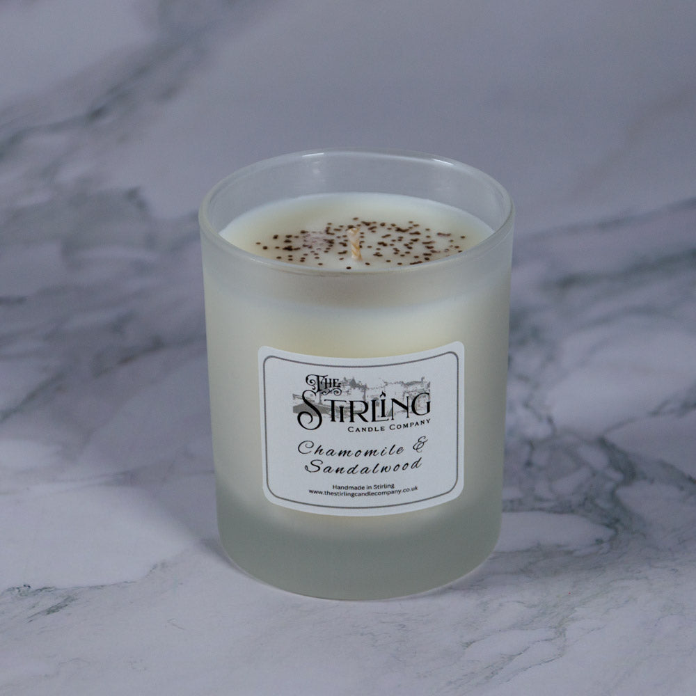 A frosted glass candle jar with white wax and black speckles labeled chamomile and sandalwood by Stirling Candle Company