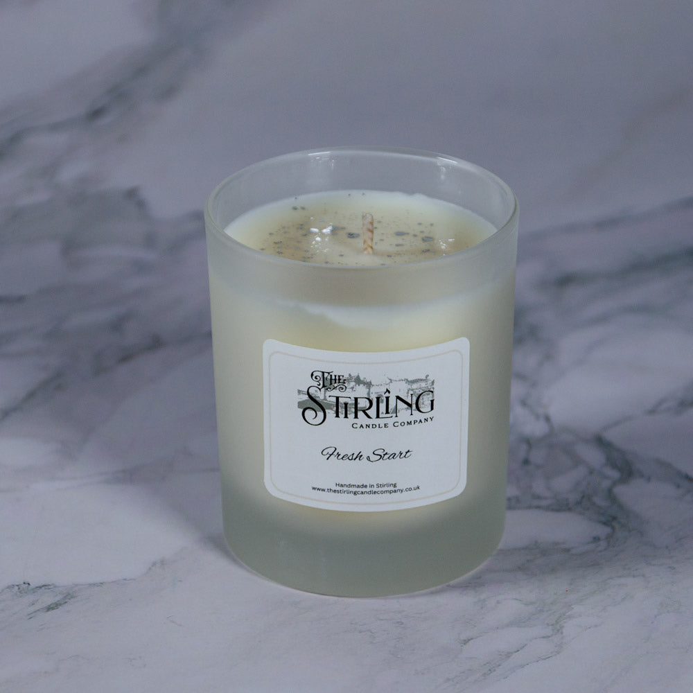 A frosted glass candle jar with creamy white wax and specks labeled fresh start by stirling candle company medium candle