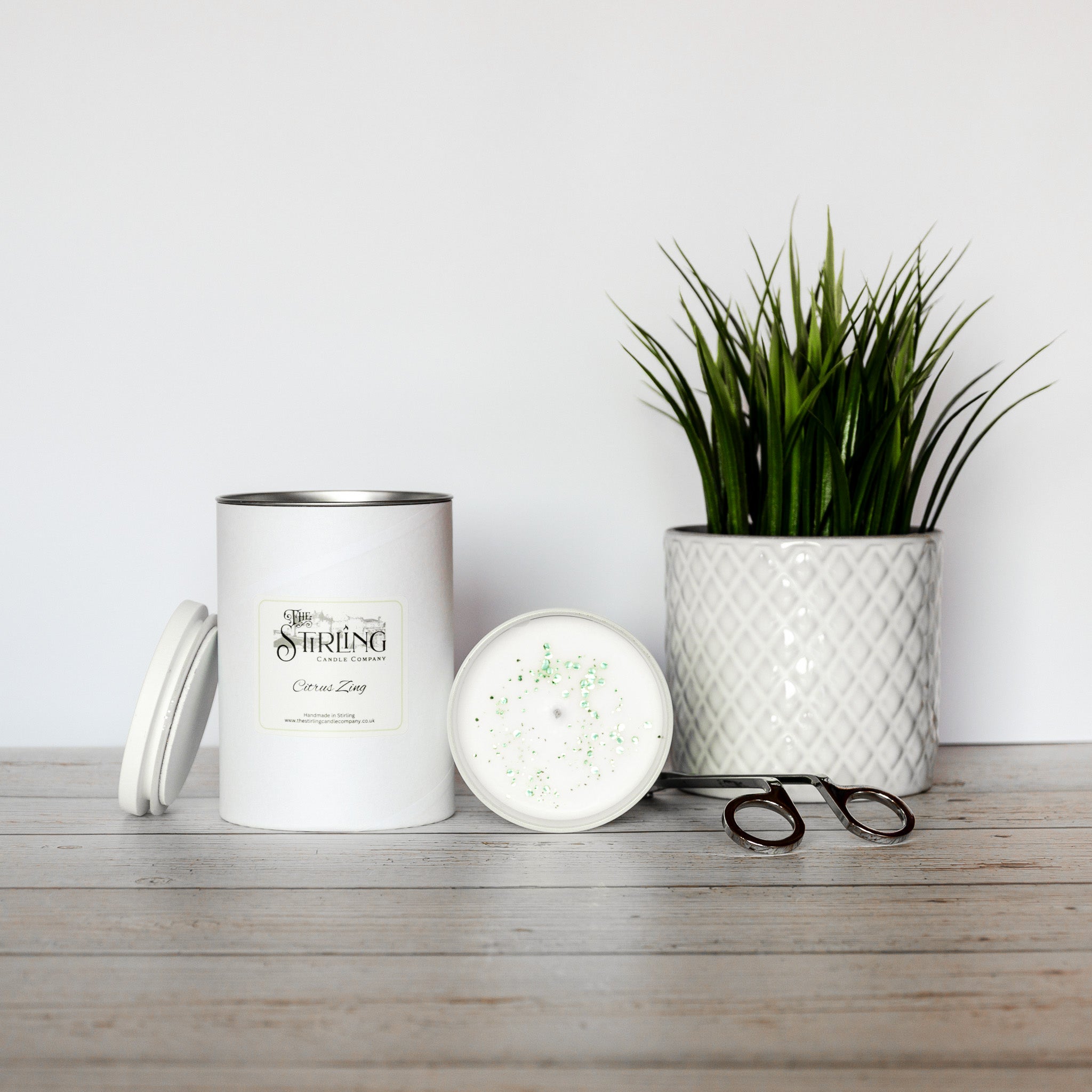 Large white cylindrical citrus zing candle by stirring candle company with silver rim and green speckles in wax