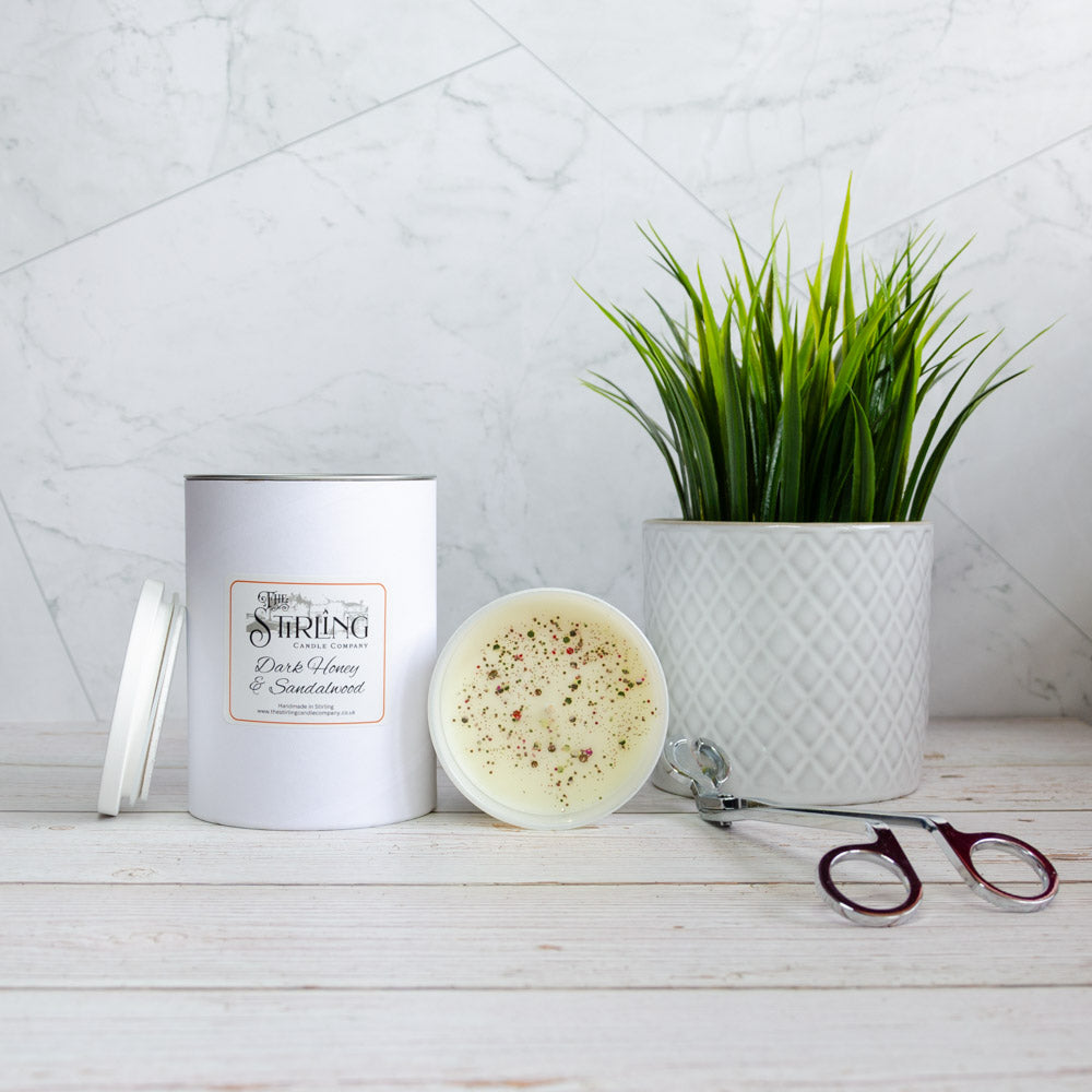 White cylindrical large candle from stirling candle company with dark honey and sandalwood scent and speckled wax