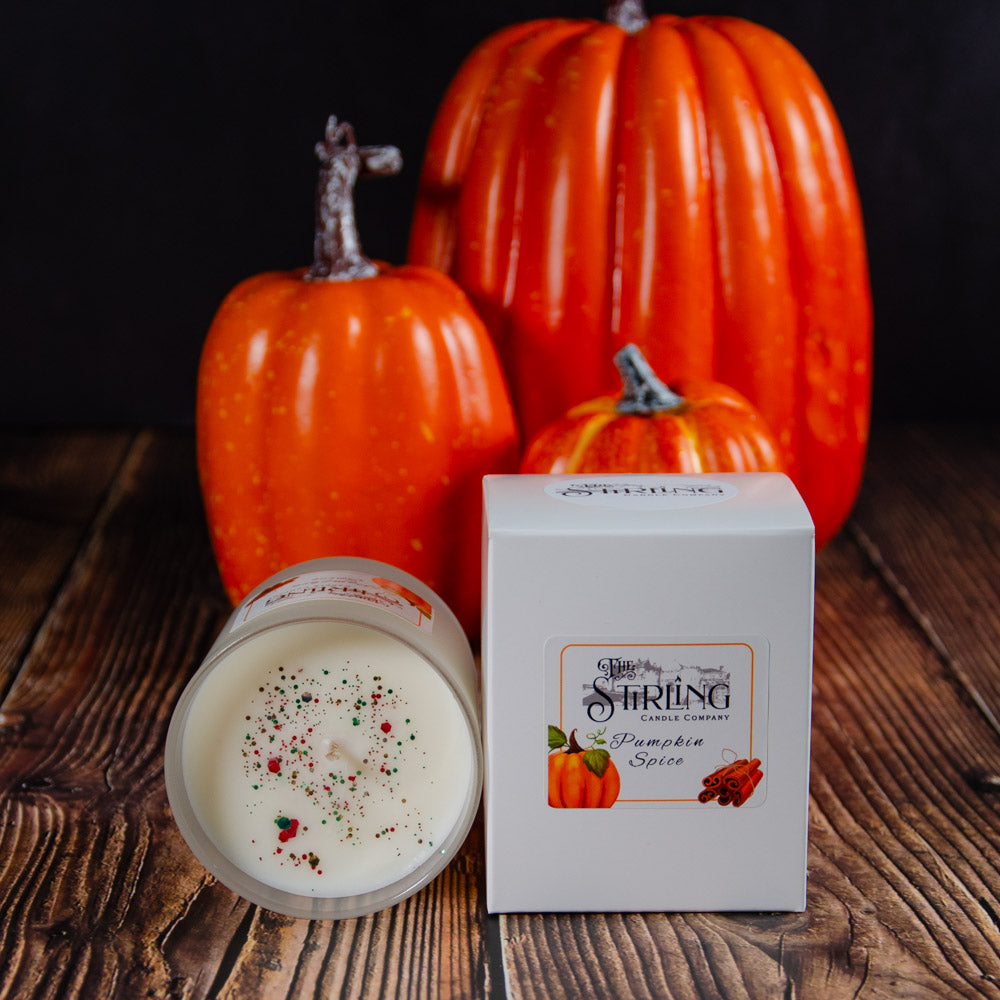 A white pumpkin spice medium candle in a clear glass jar with colorful speckles next to its branded box