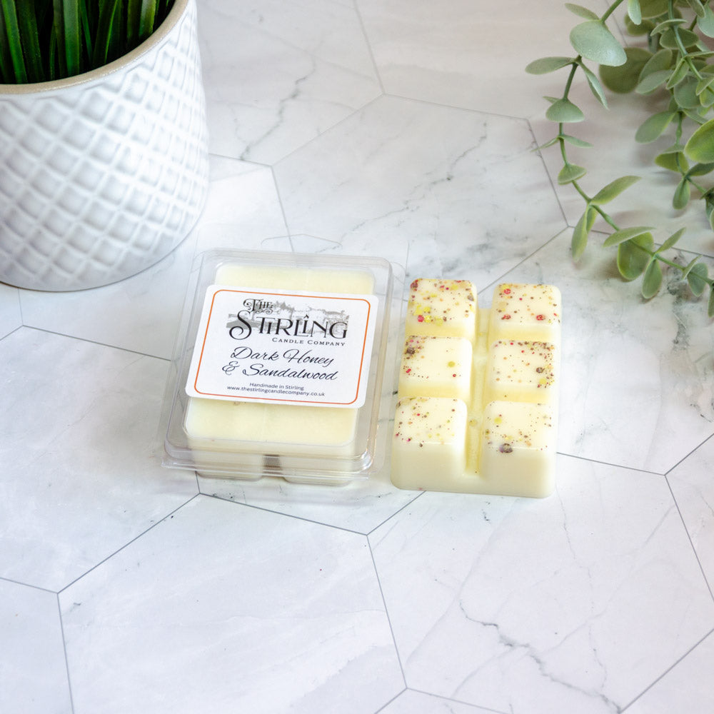 Cream-colored wax melts with red and green speckles in clear clamshell from the string candle company dark honey and sandalwood