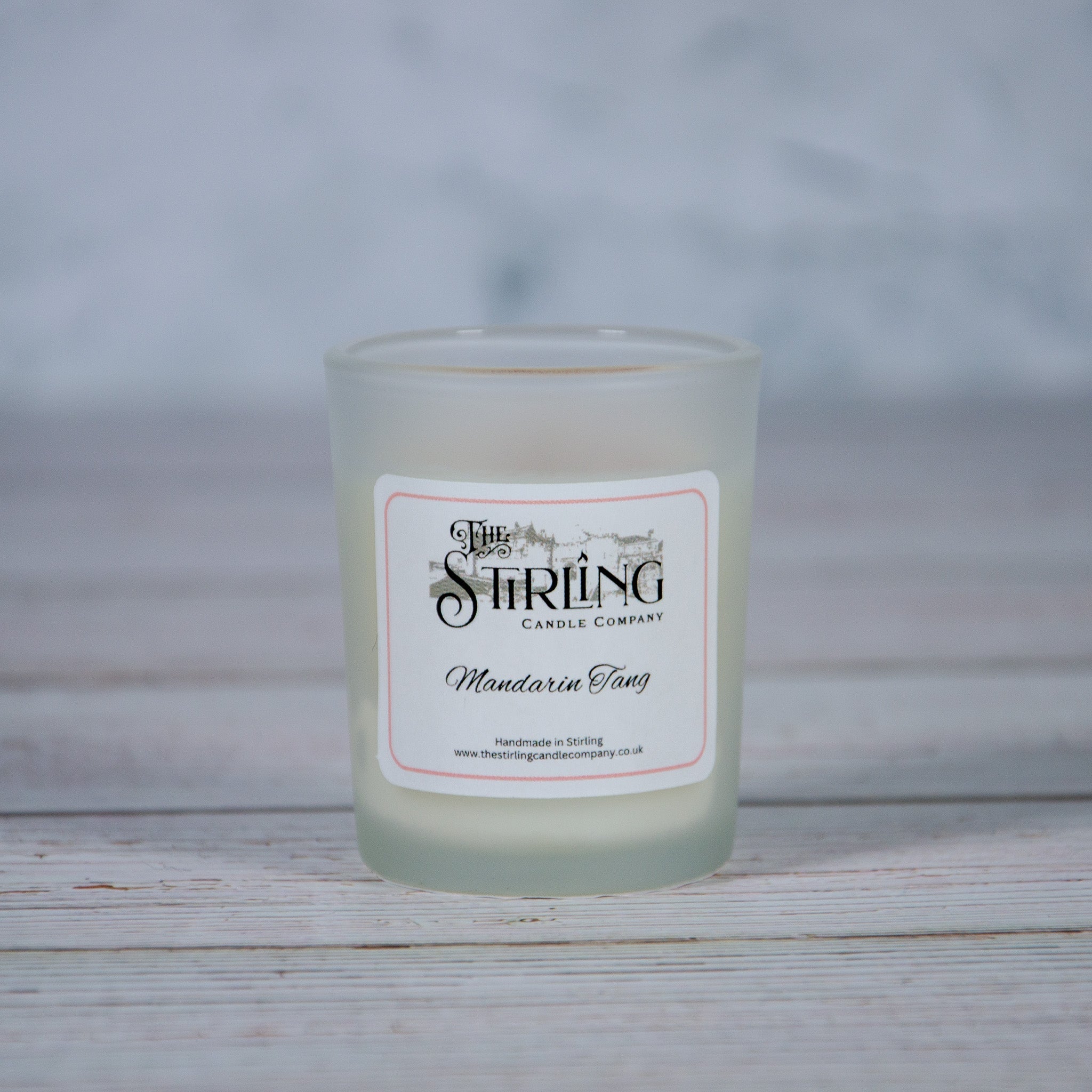 A frosted glass small candle jar with a white label and pink border labeled mandarin tang by the string candle company