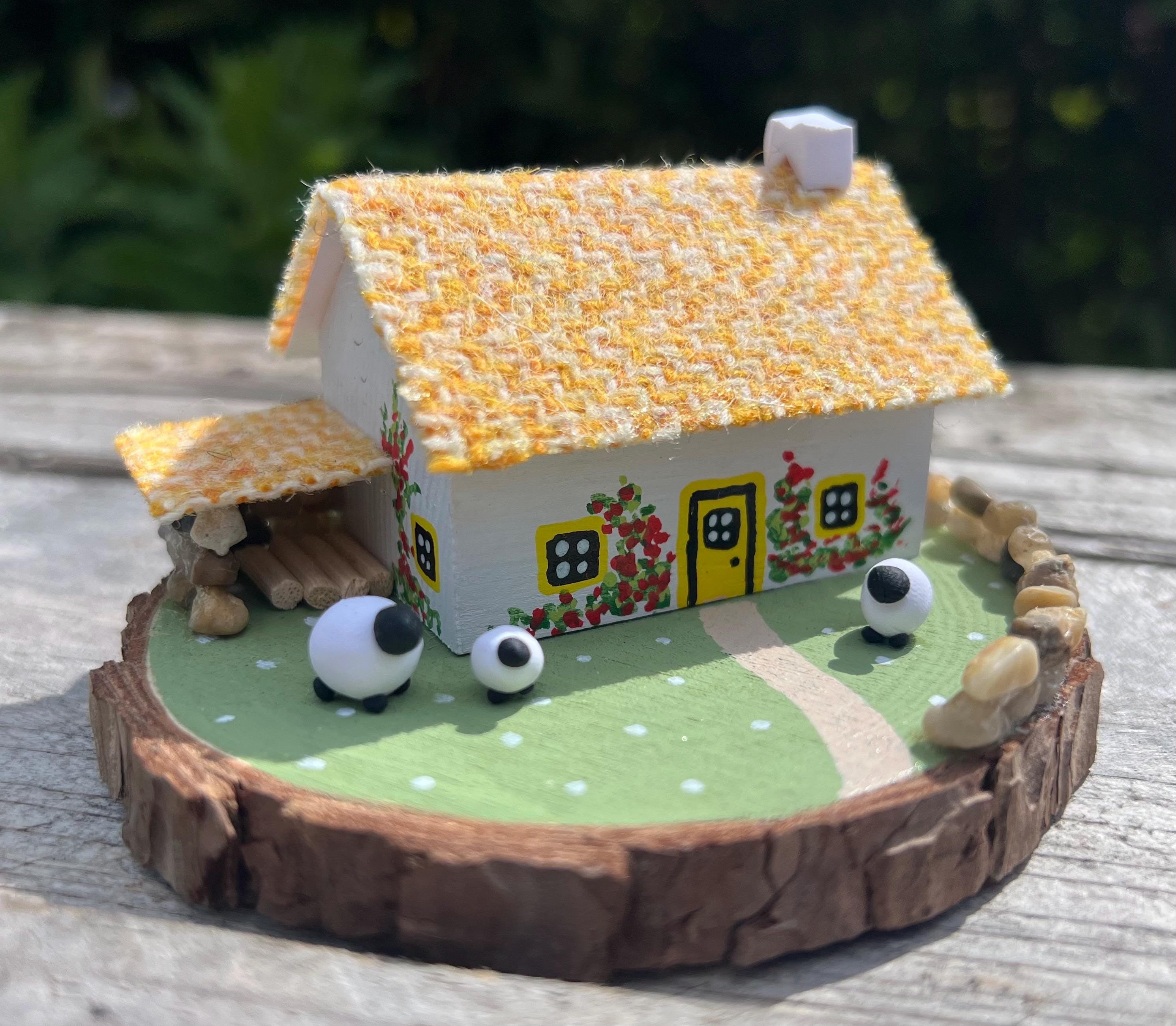 Handcrafted miniature Scottish Bothy with thatched roof, red roses, yellow windows, and sheep figurines on wood base