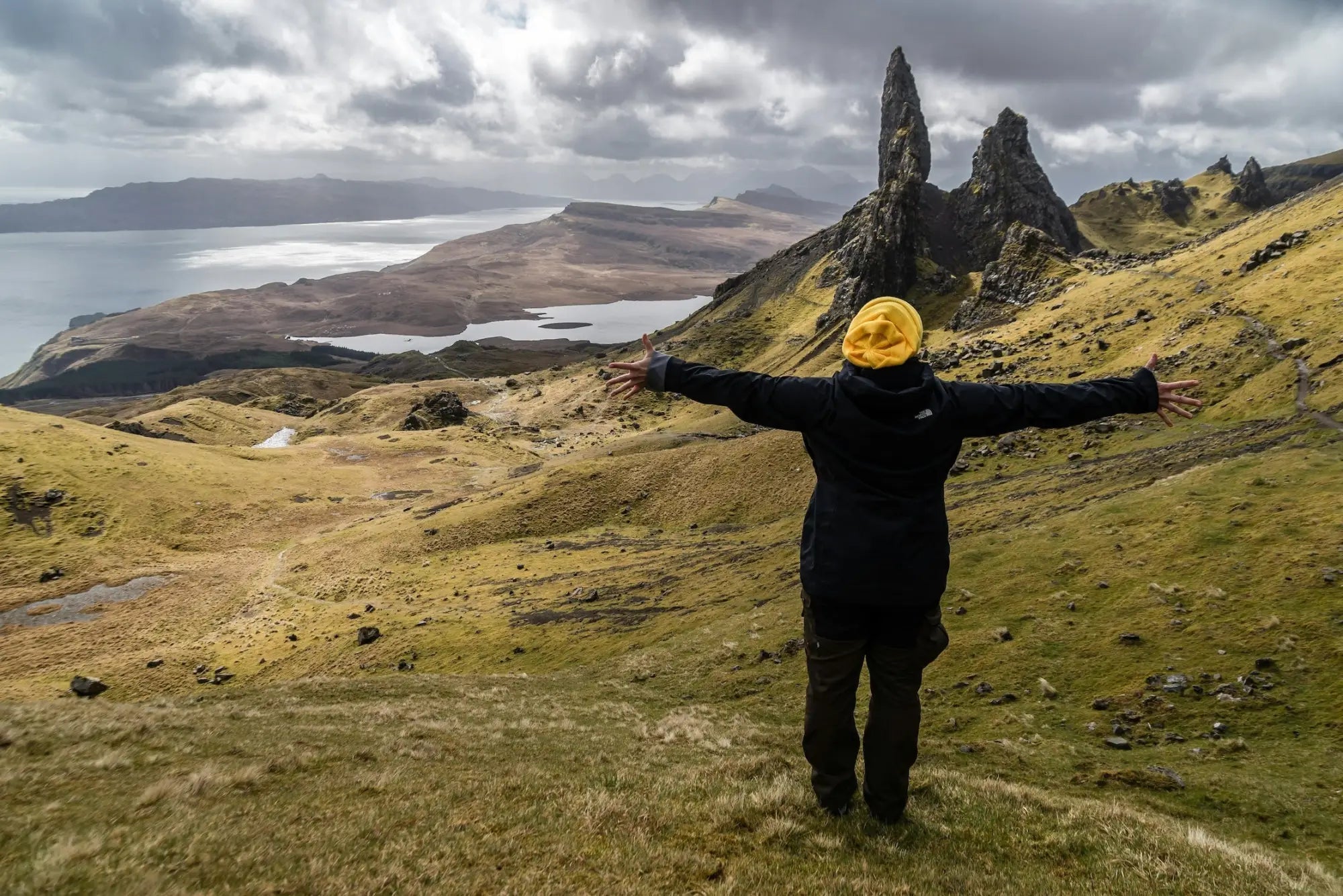 Person in black jacket and yellow beanie facing scenic mountain landscape at Guest Artists Gallery
