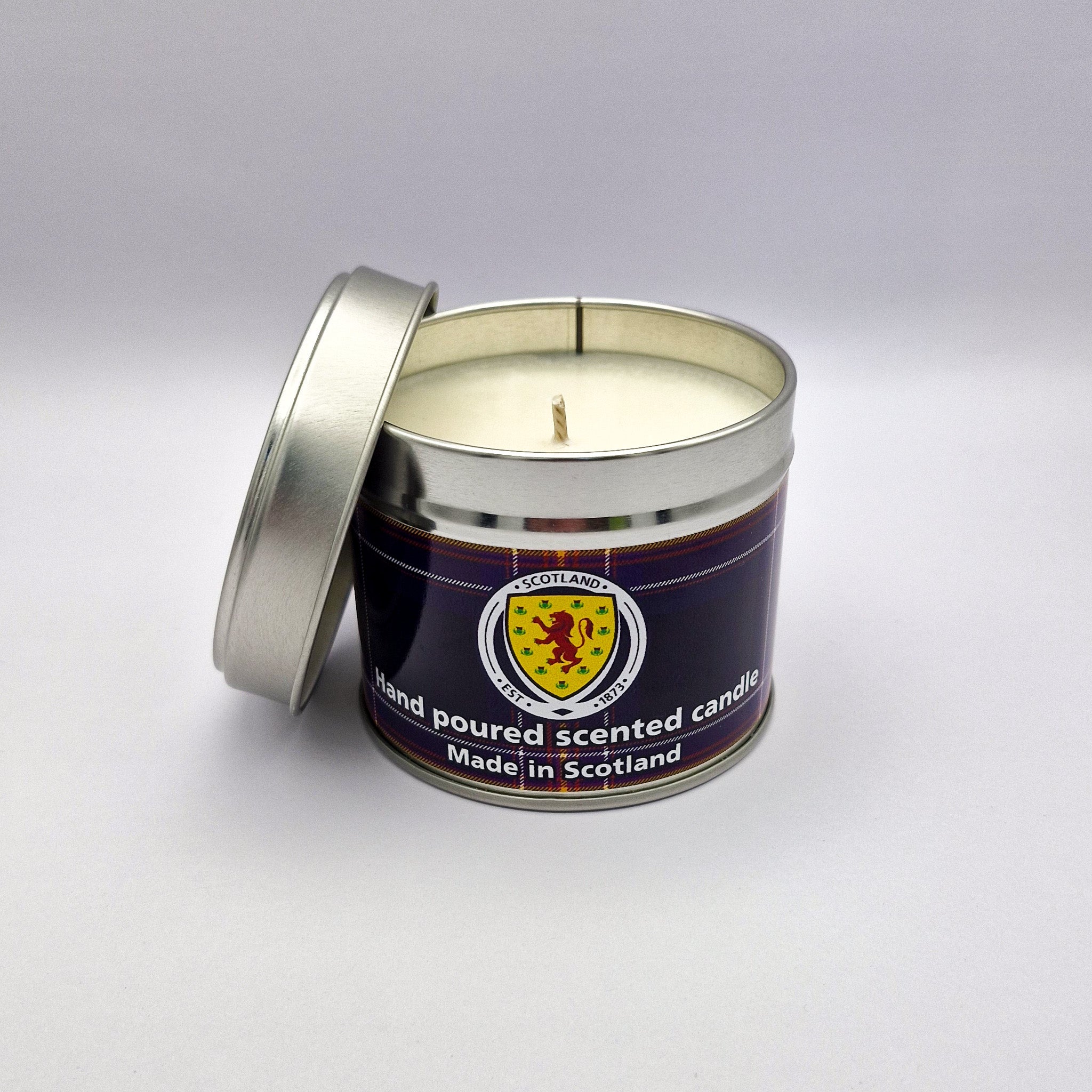 A hand-poured scented travel tin candle with creamy white wax and a dark blue scottish crest label