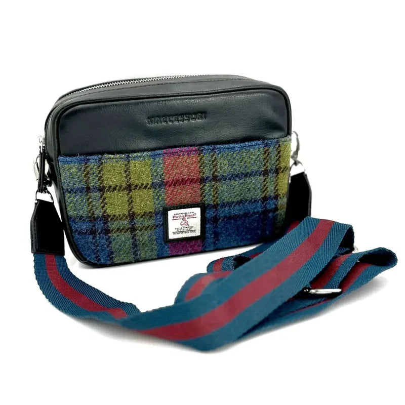 A small crossbody bag featuring a plaid wool front and black leather back with a striped adjustable strap.