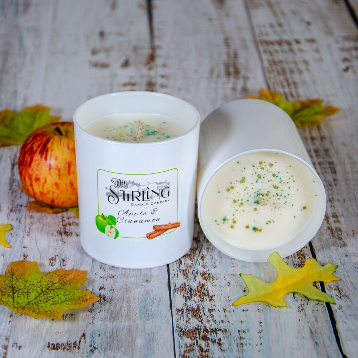 Apple & Cinnamon large candle with its lid off, showing dried botanicals on the wax, with autumn leaves