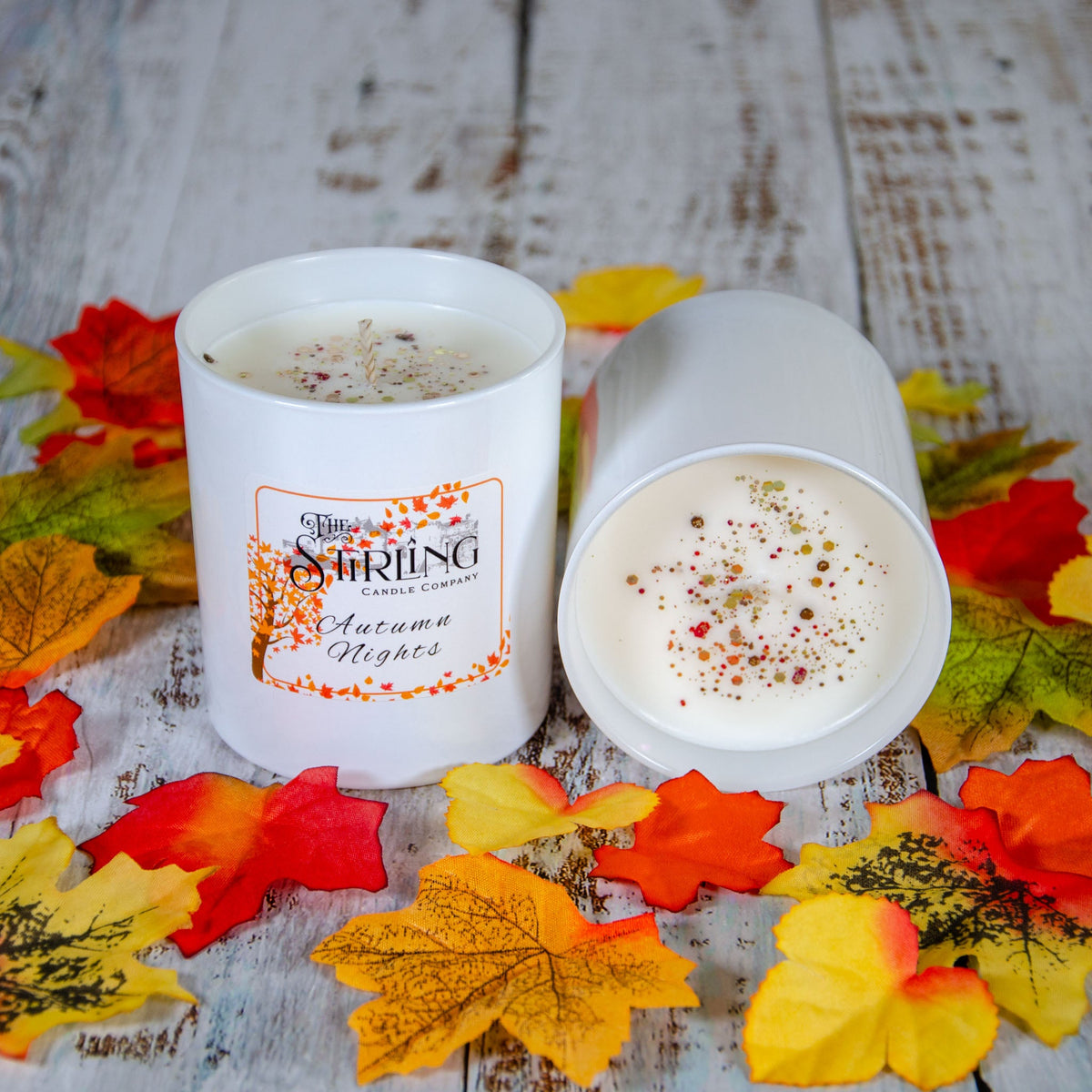 Two Autumn Nights large candles, one showing dried botanicals on the wax, with autumn leaves