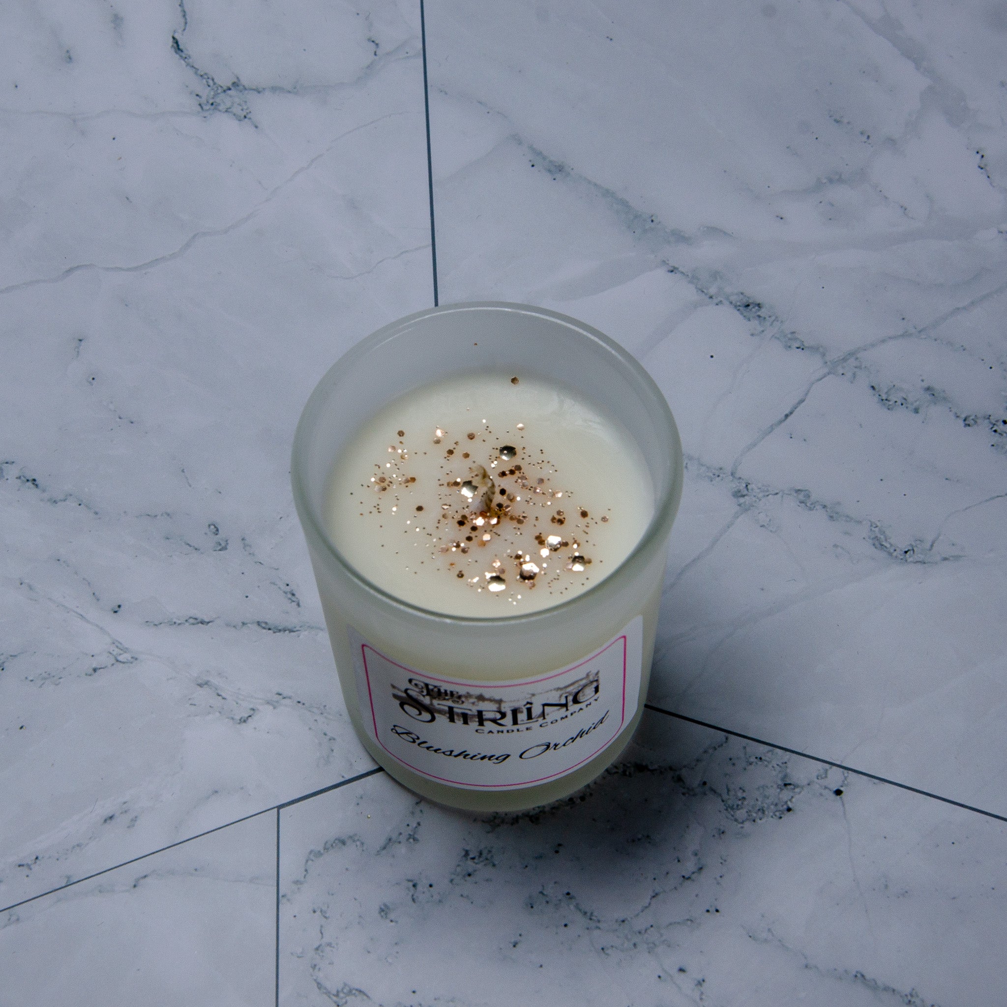 Blushing orchid small candle is a white scented candle in a clear glass jar with gold glitter from charming candle co